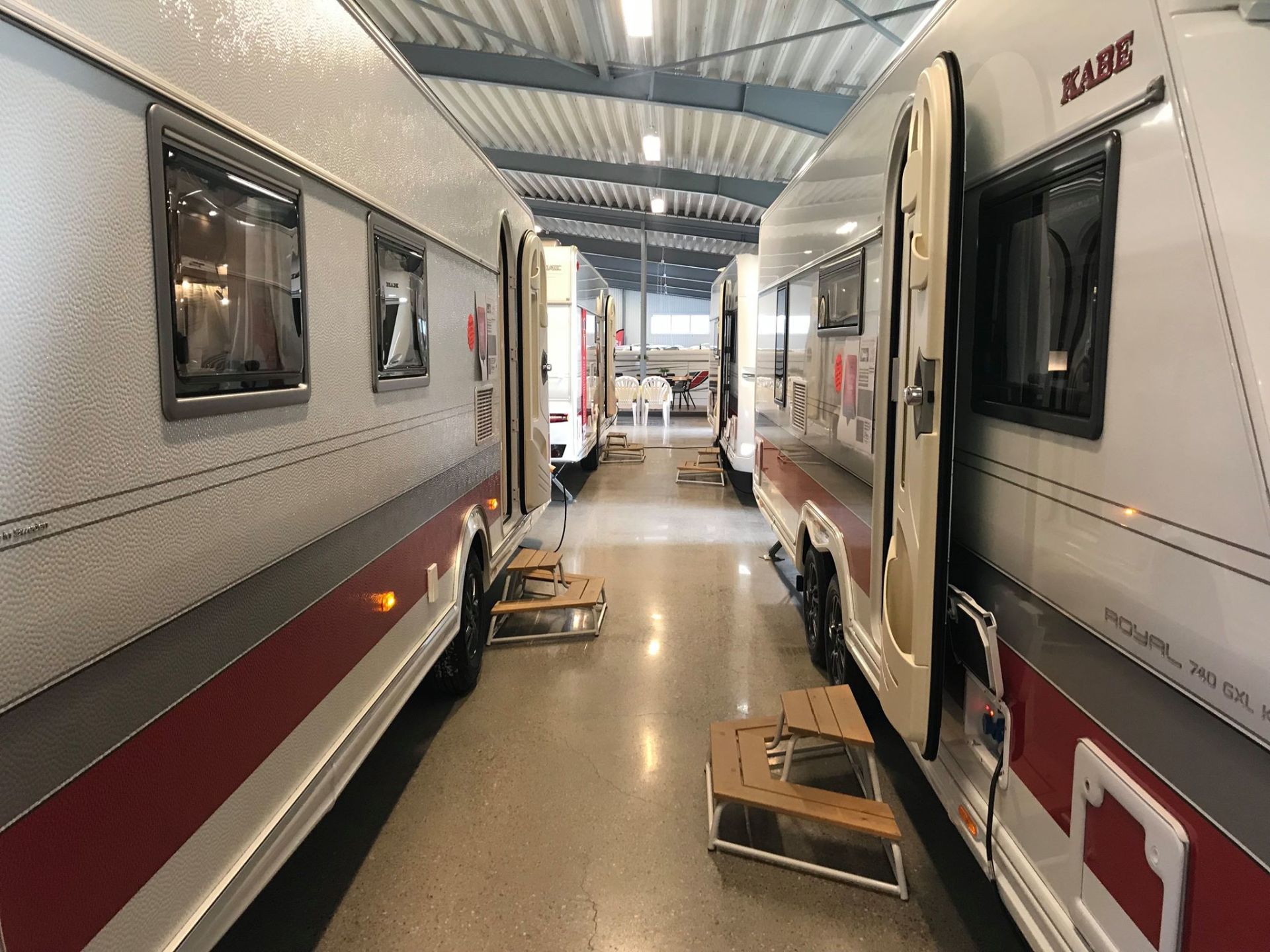 Two travel trailers parked closely together inside a brightly lit garage.