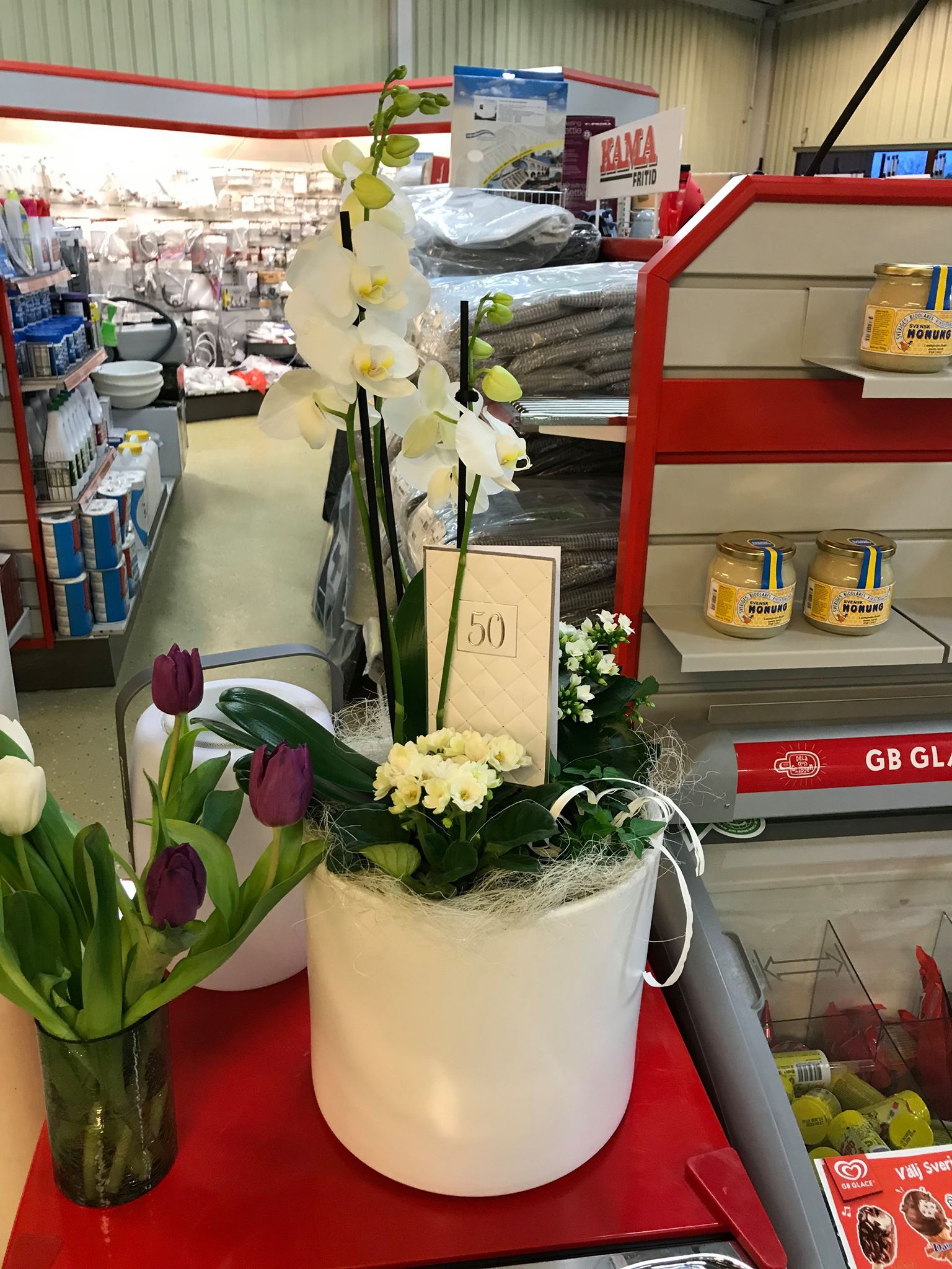 White orchid and tulips in a store; display of flowers and other products on shelves.