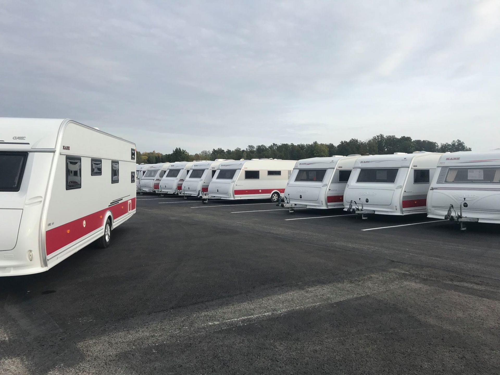 Row of white and red caravans parked on asphalt. Overcast sky in background.
