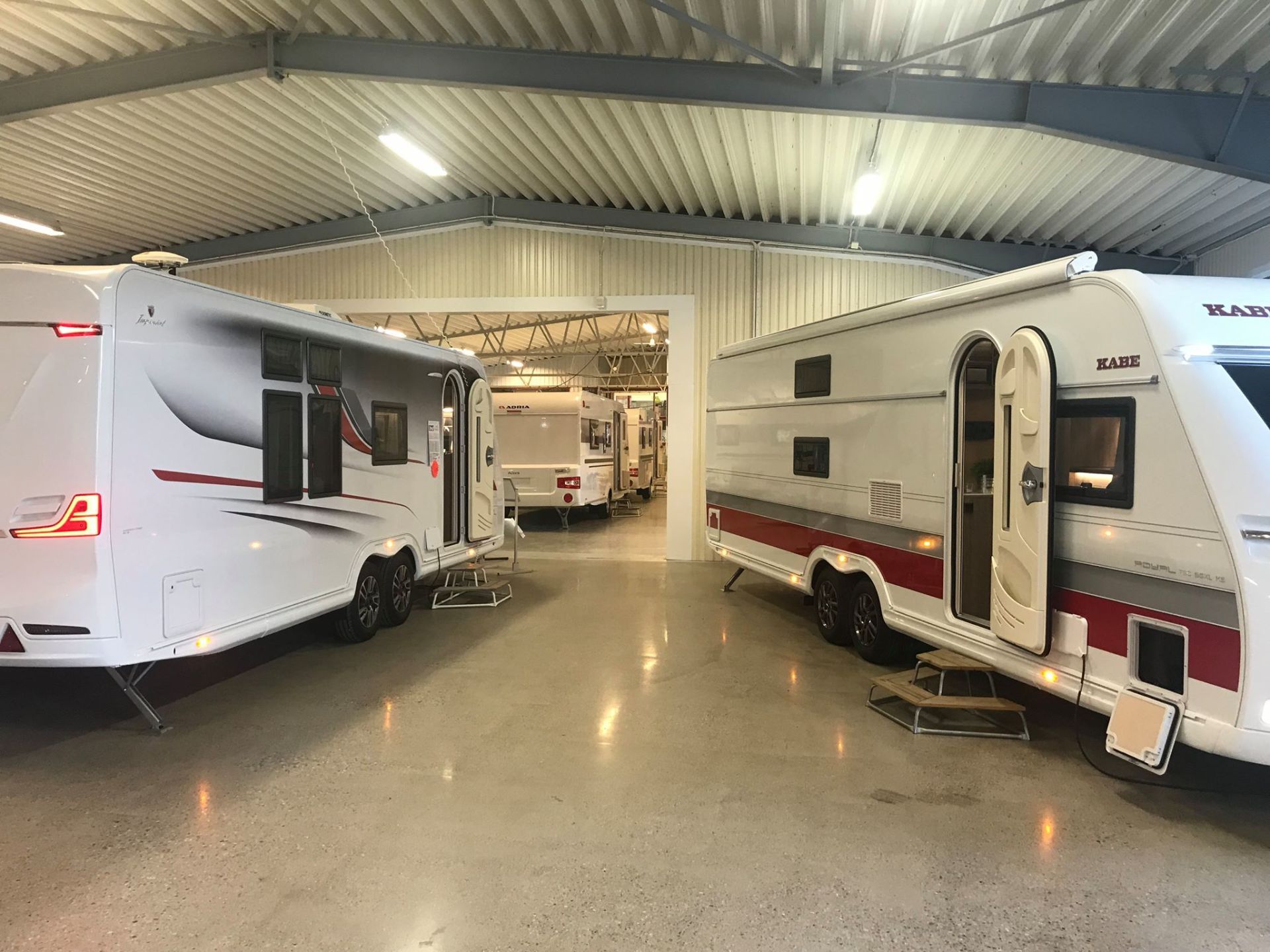 Several white RV trailers parked inside a warehouse with open doors.