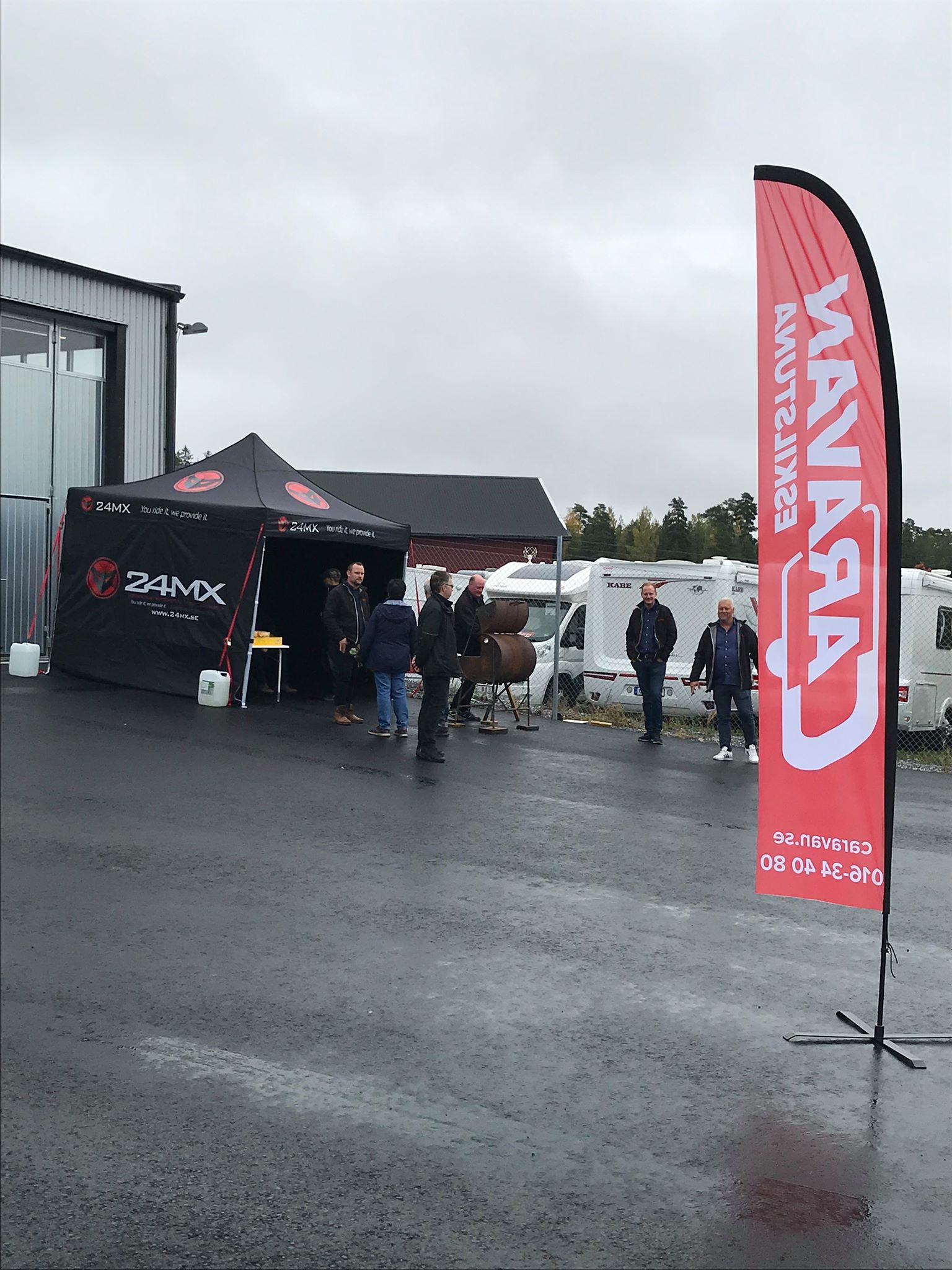 People at an outdoor event with a branded tent and flag; overcast day.