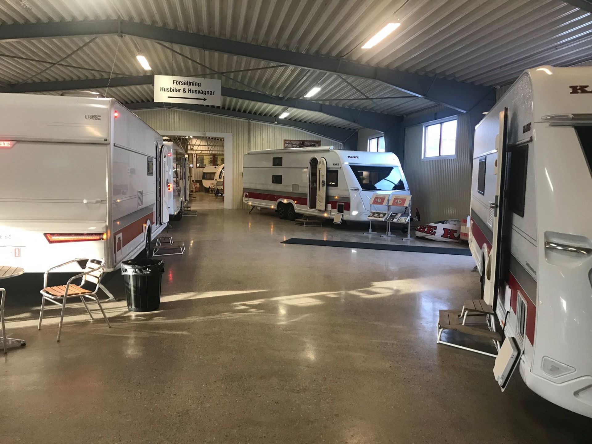Indoor shot of a caravan showroom. Several white caravans with red stripes are on display, under fluorescent lights.