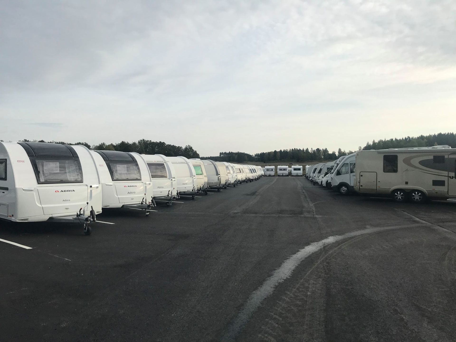 Rows of white travel trailers parked on a paved lot under a cloudy sky.
