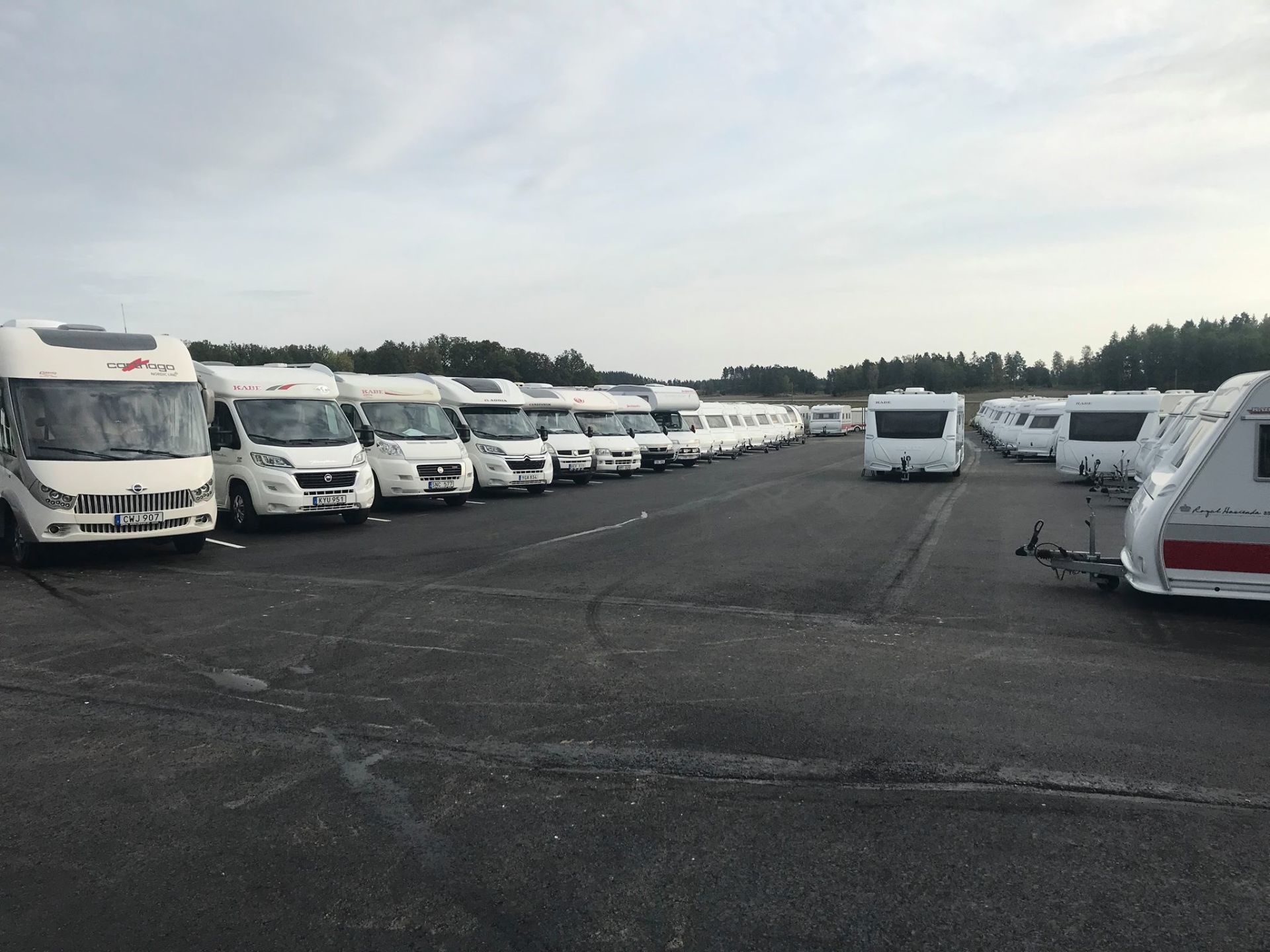 Rows of white RVs and trailers parked on an asphalt lot under a cloudy sky.