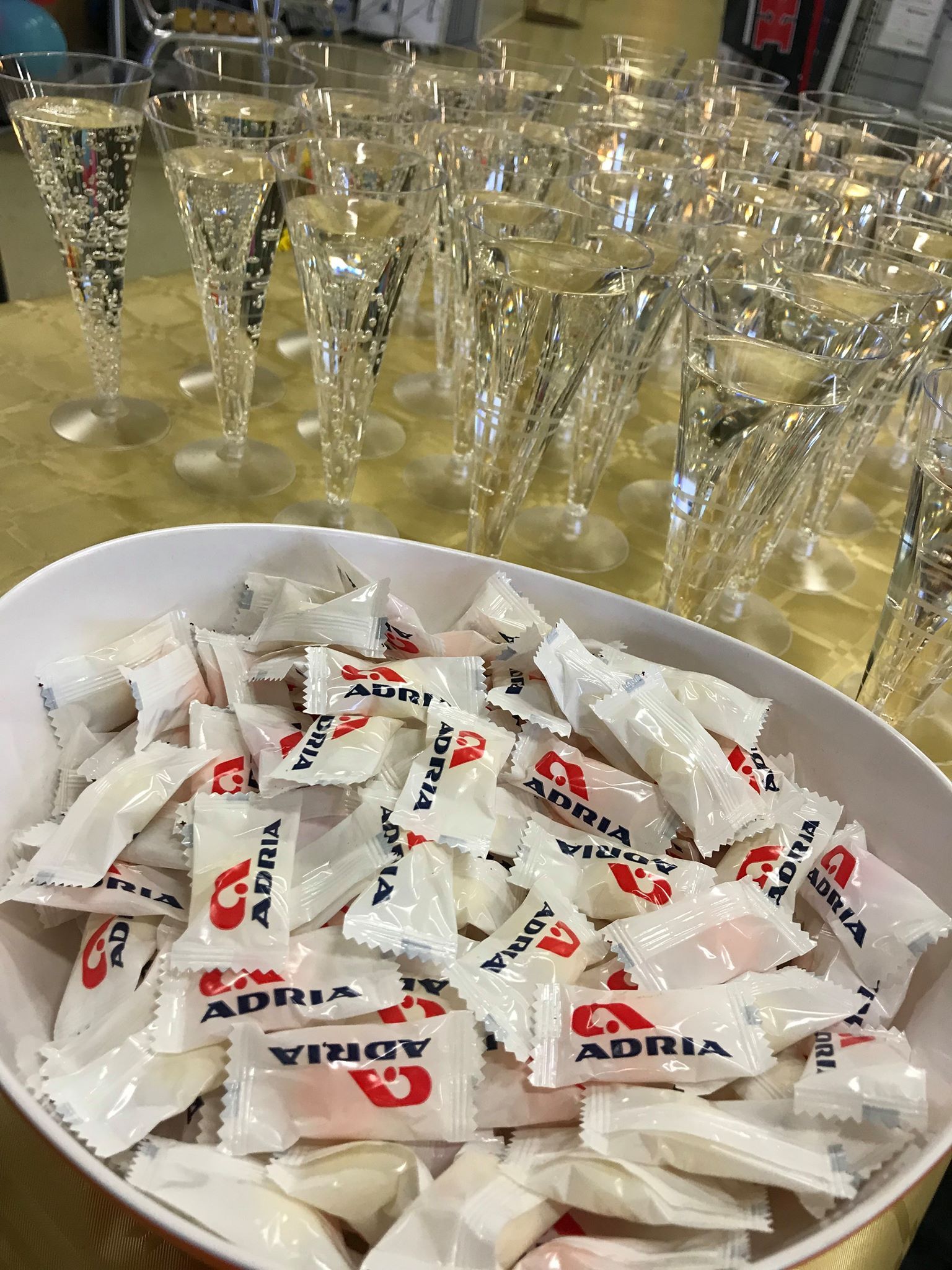 Bowl of wrapped candies with red logo in front of champagne flutes.