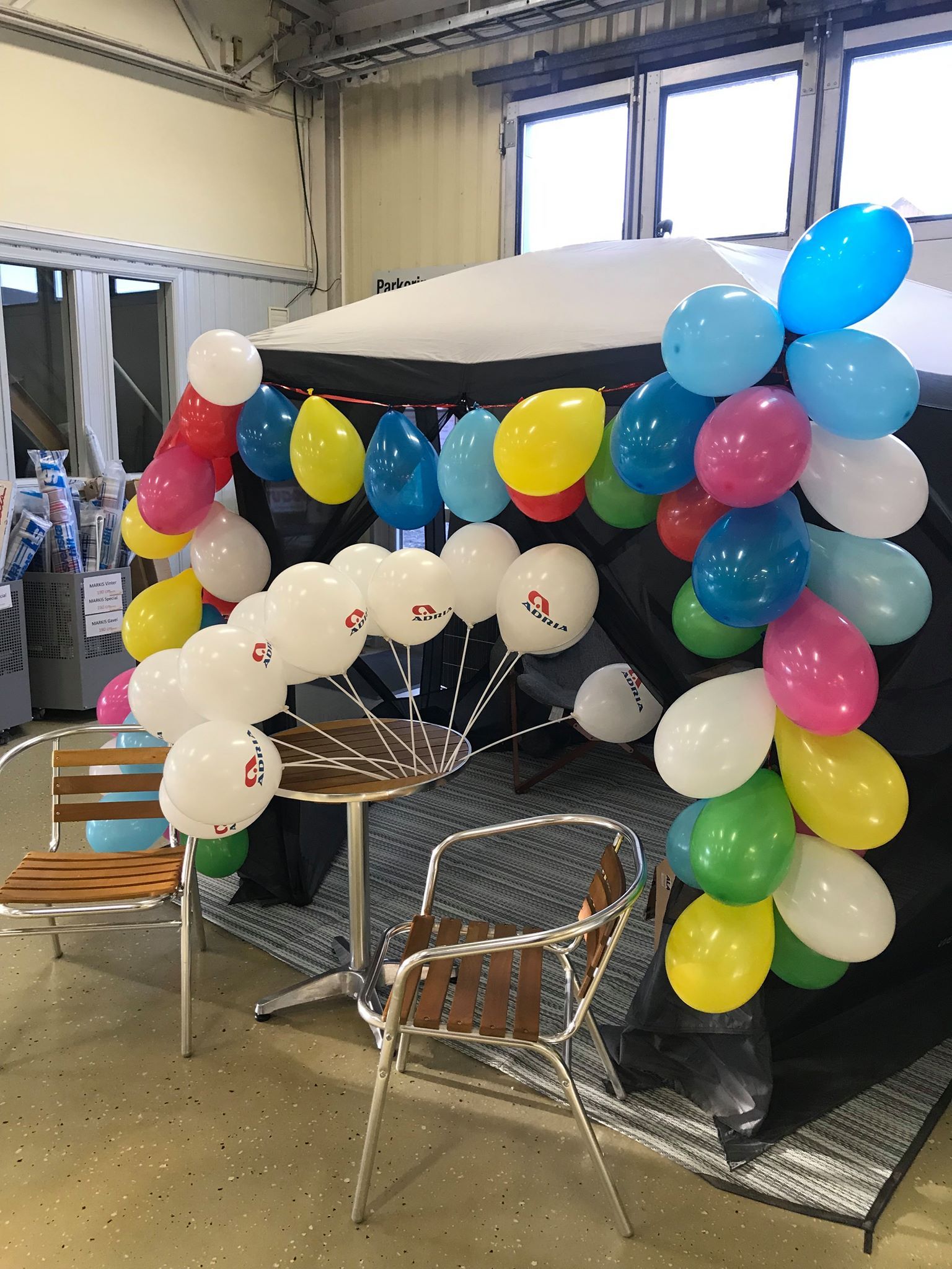 Balloons in various colors decorate a tent with a table and chairs in an indoor setting.