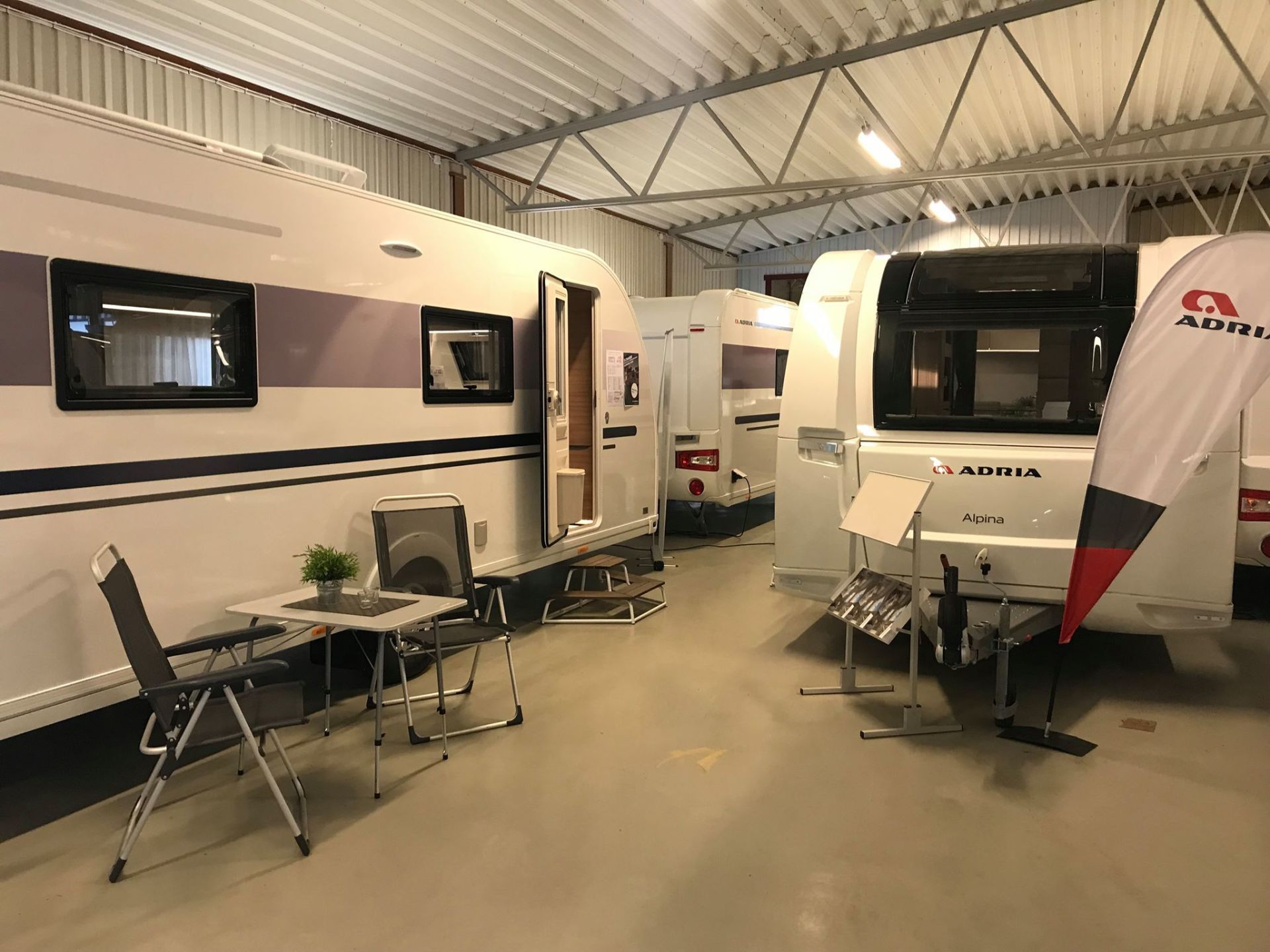 Caravans on display inside a brightly lit showroom; a table and chairs sit outside one.