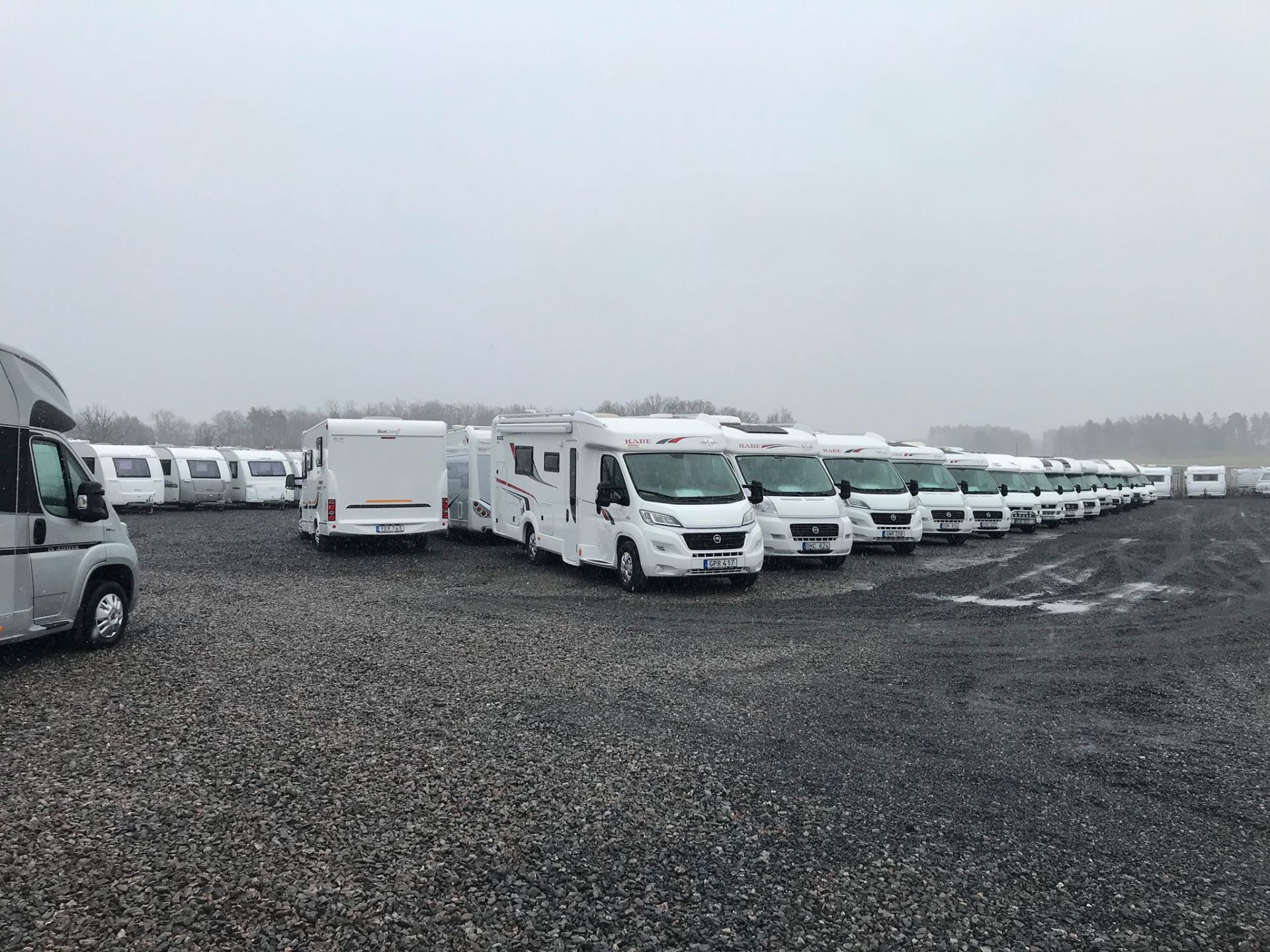 Rows of white RVs parked on a gravel lot under an overcast sky.