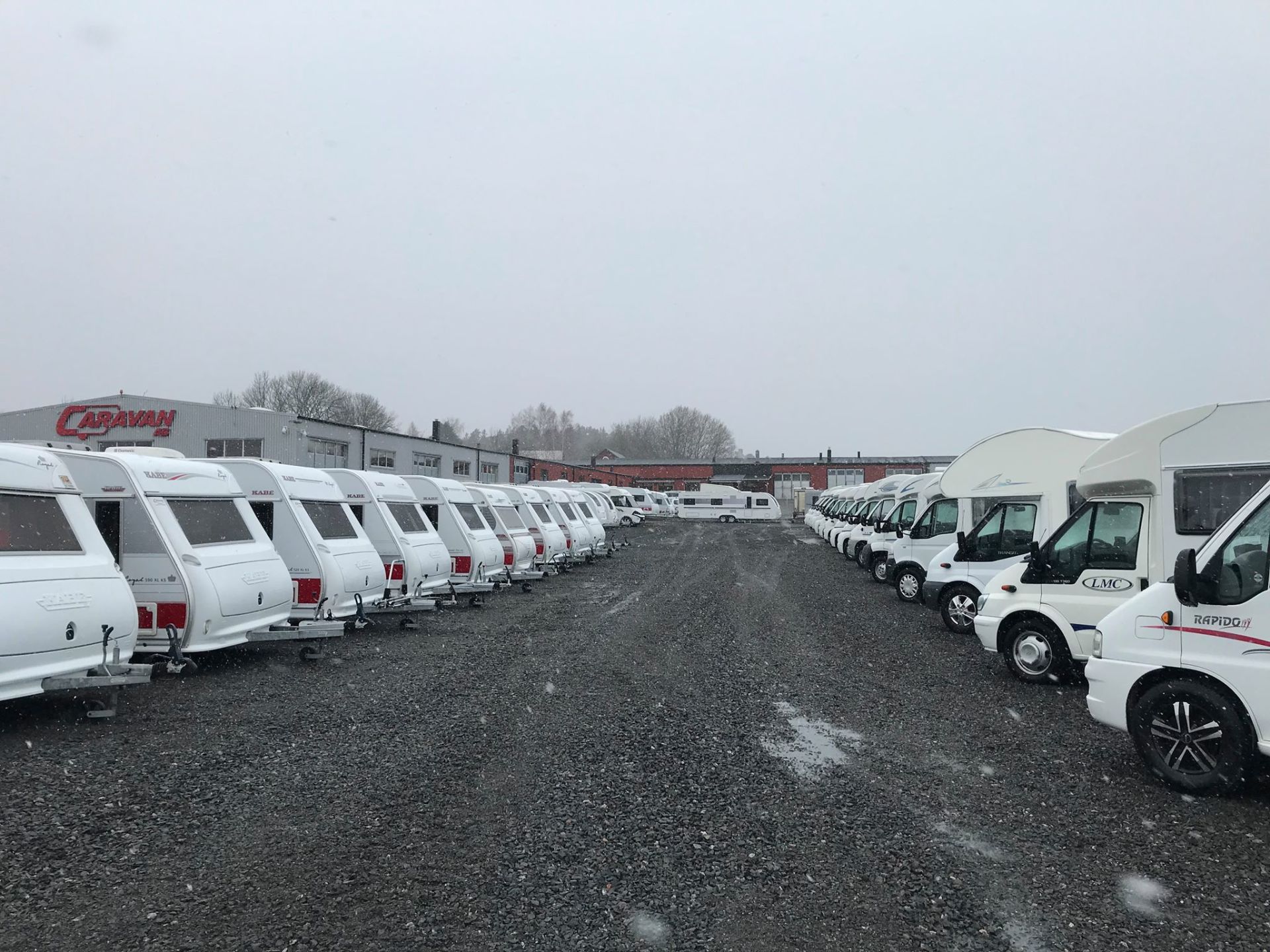 Rows of white RVs and trailers parked in a lot under a cloudy sky.