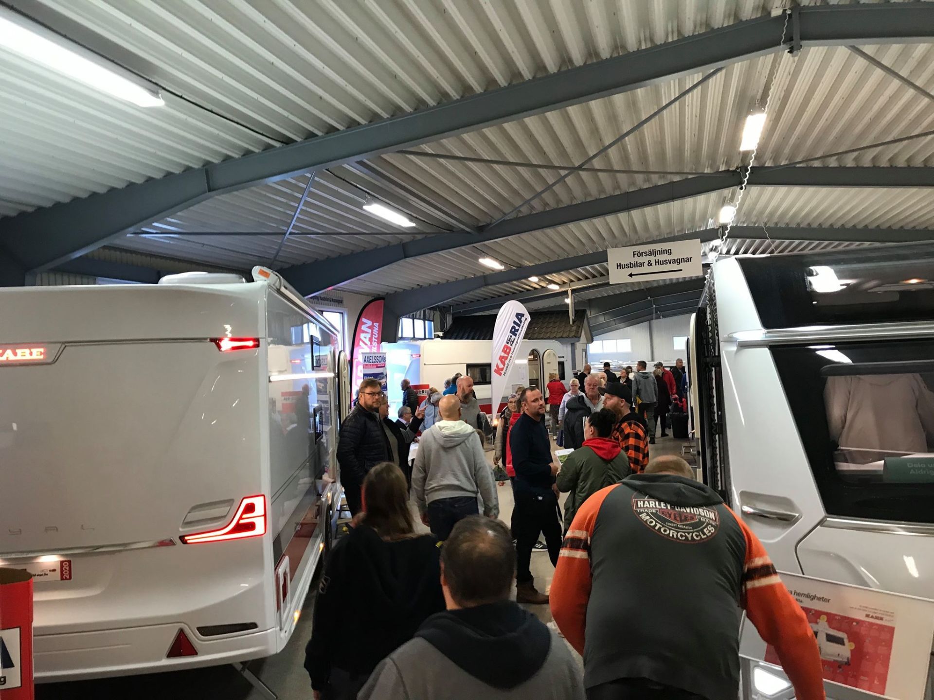 People browse RVs inside a large building with bright lighting.