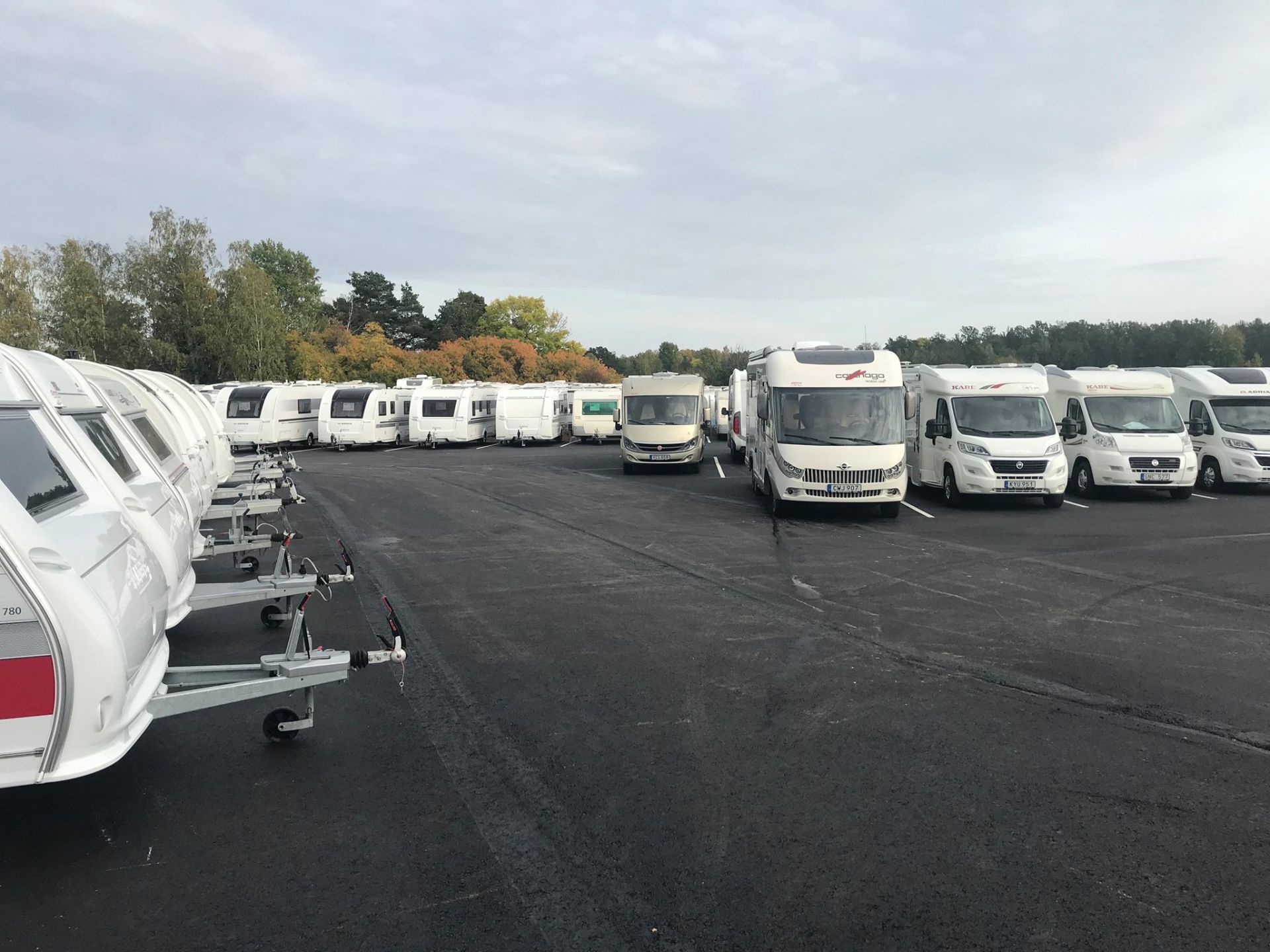 Campers and trailers parked on asphalt. Cloudy sky in the background.