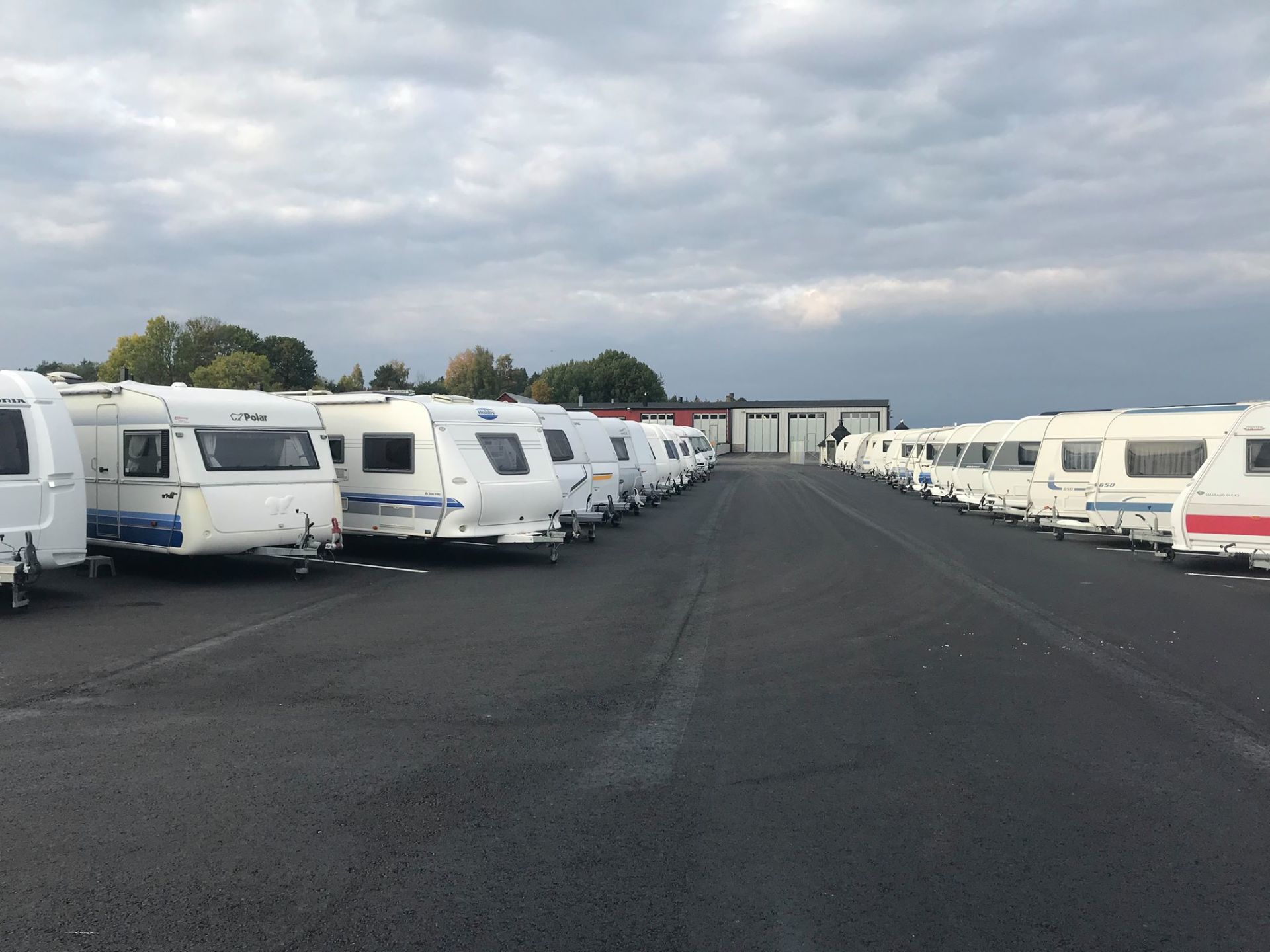 Rows of white caravans parked on asphalt under a cloudy sky.