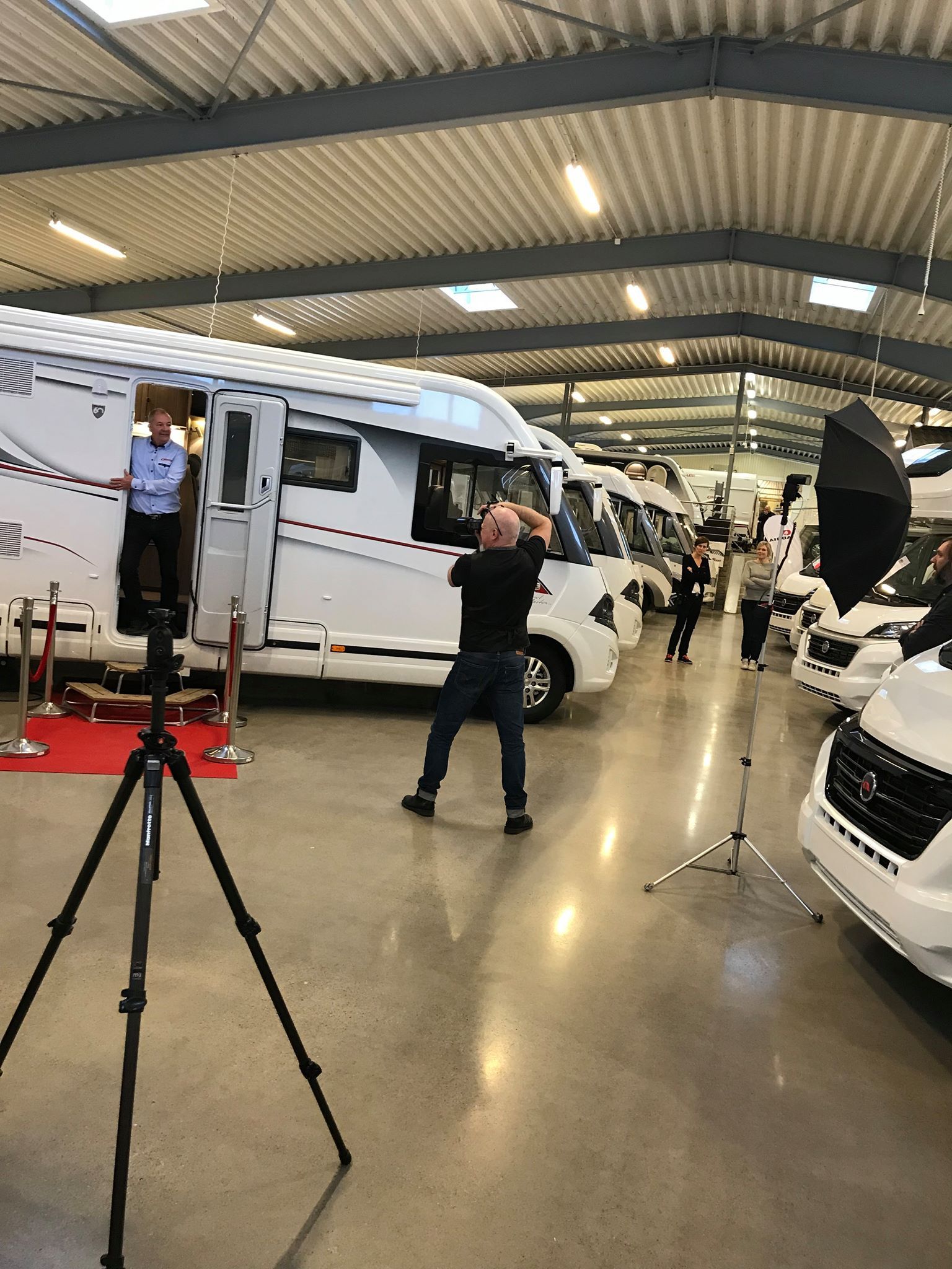 A person photographs a child standing in the doorway of a white RV at a car show. Other RVs are visible.