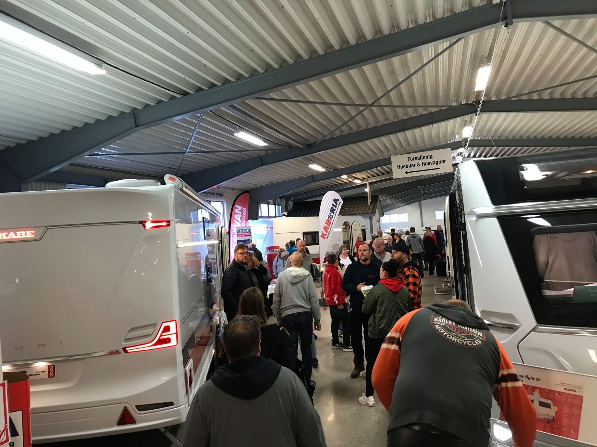 People browsing caravans inside a building. Bright lighting and many people.