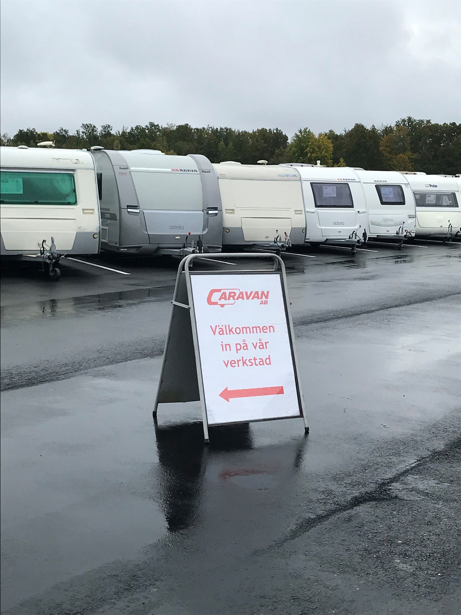 A-frame sign with an arrow in front of a row of caravans on a wet day.