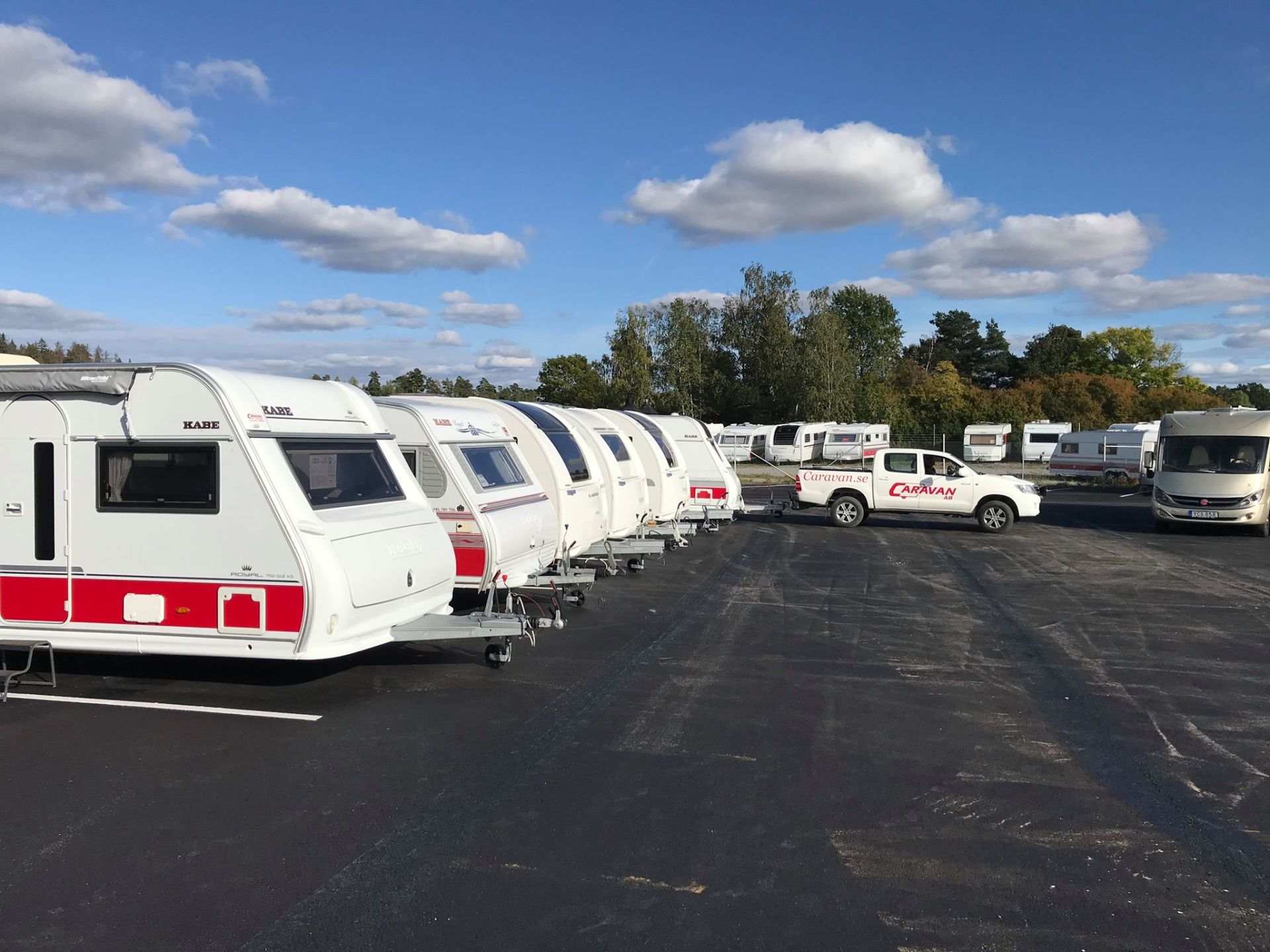 White RVs parked in a lot under a blue sky with clouds. A white pickup truck is parked nearby.