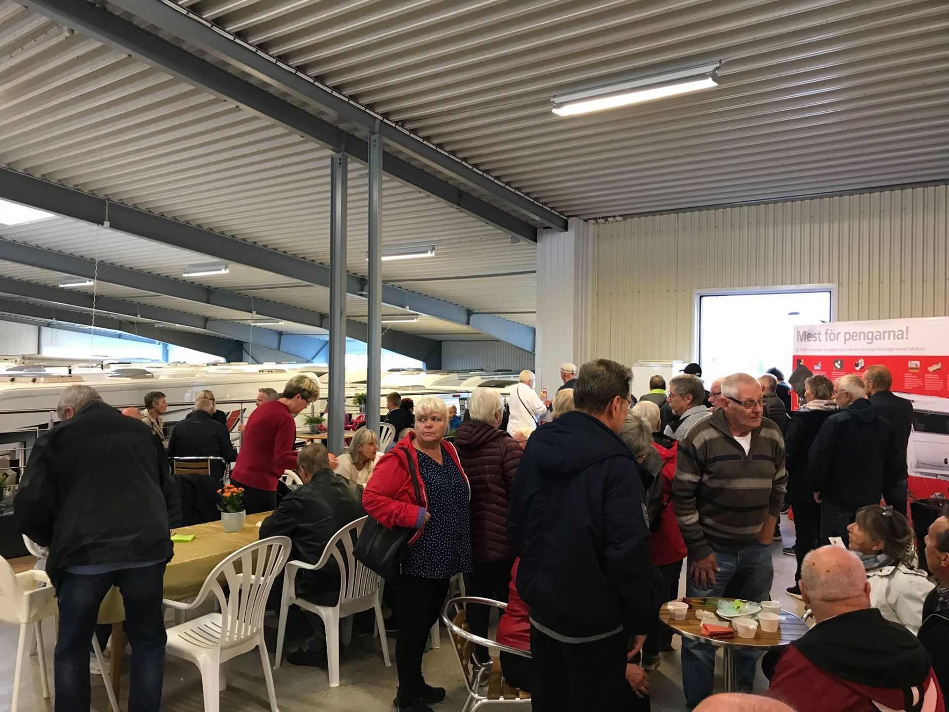 People gathered in a large indoor space, possibly an event or market, with tables, and booths visible in the background.