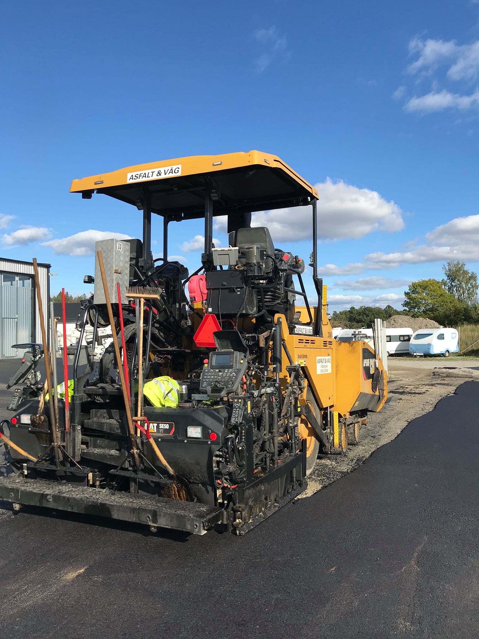 Yellow asphalt paving machine laying new pavement on a sunny day.