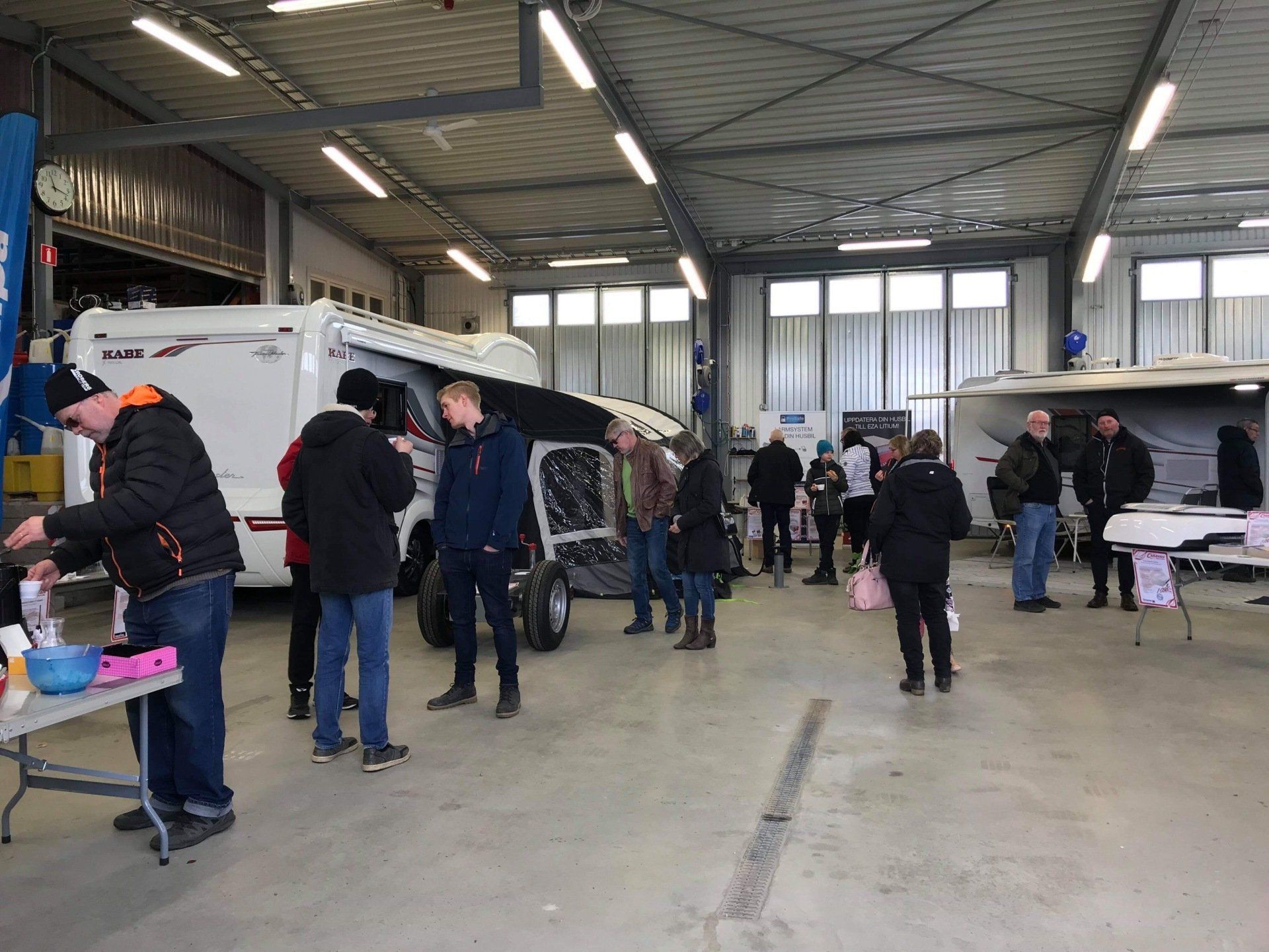 People gather inside a large garage-like building; a small electric vehicle is in the center.