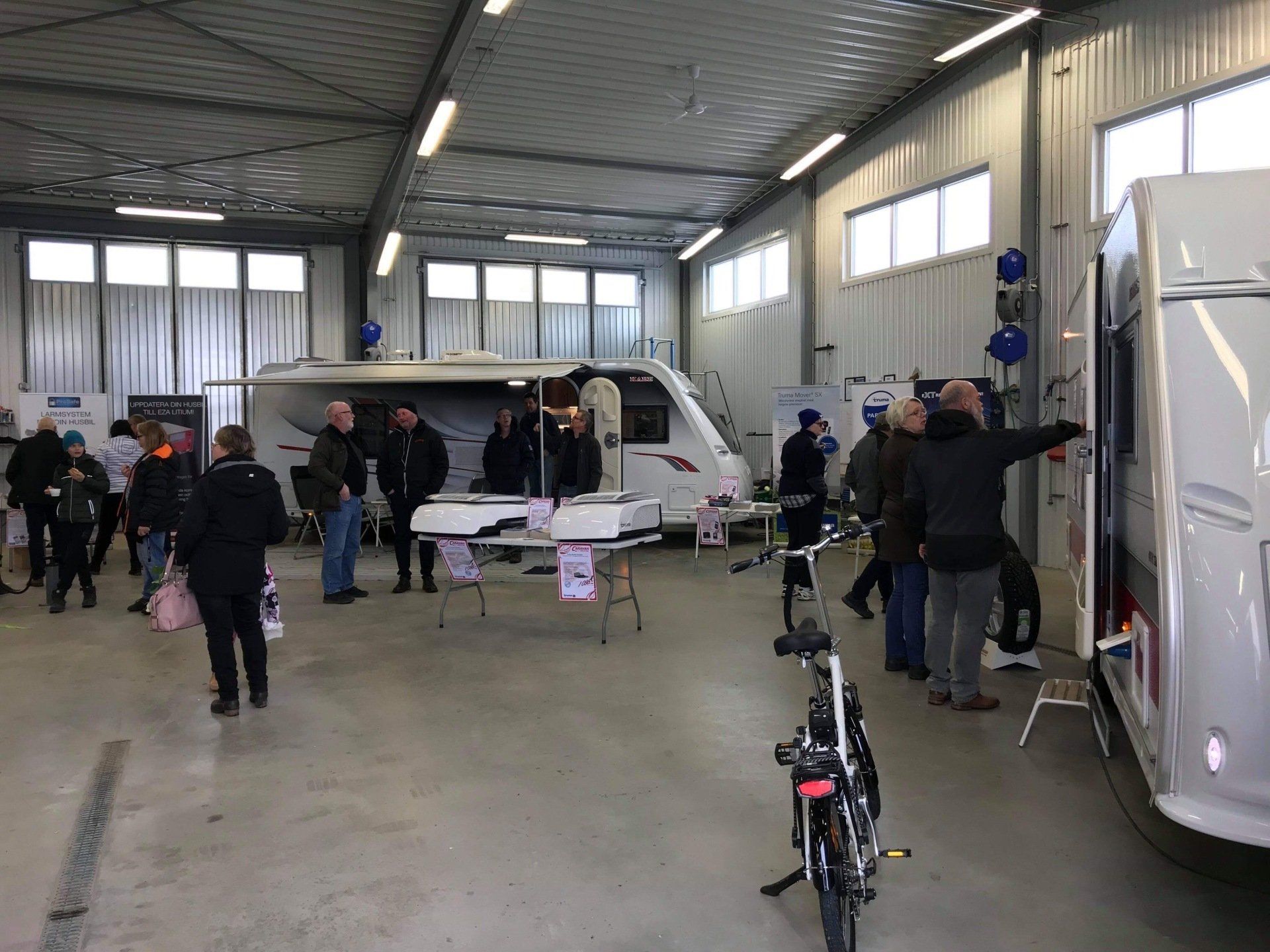 People browsing inside a large hall at a caravan show, looking at campers and brochures.