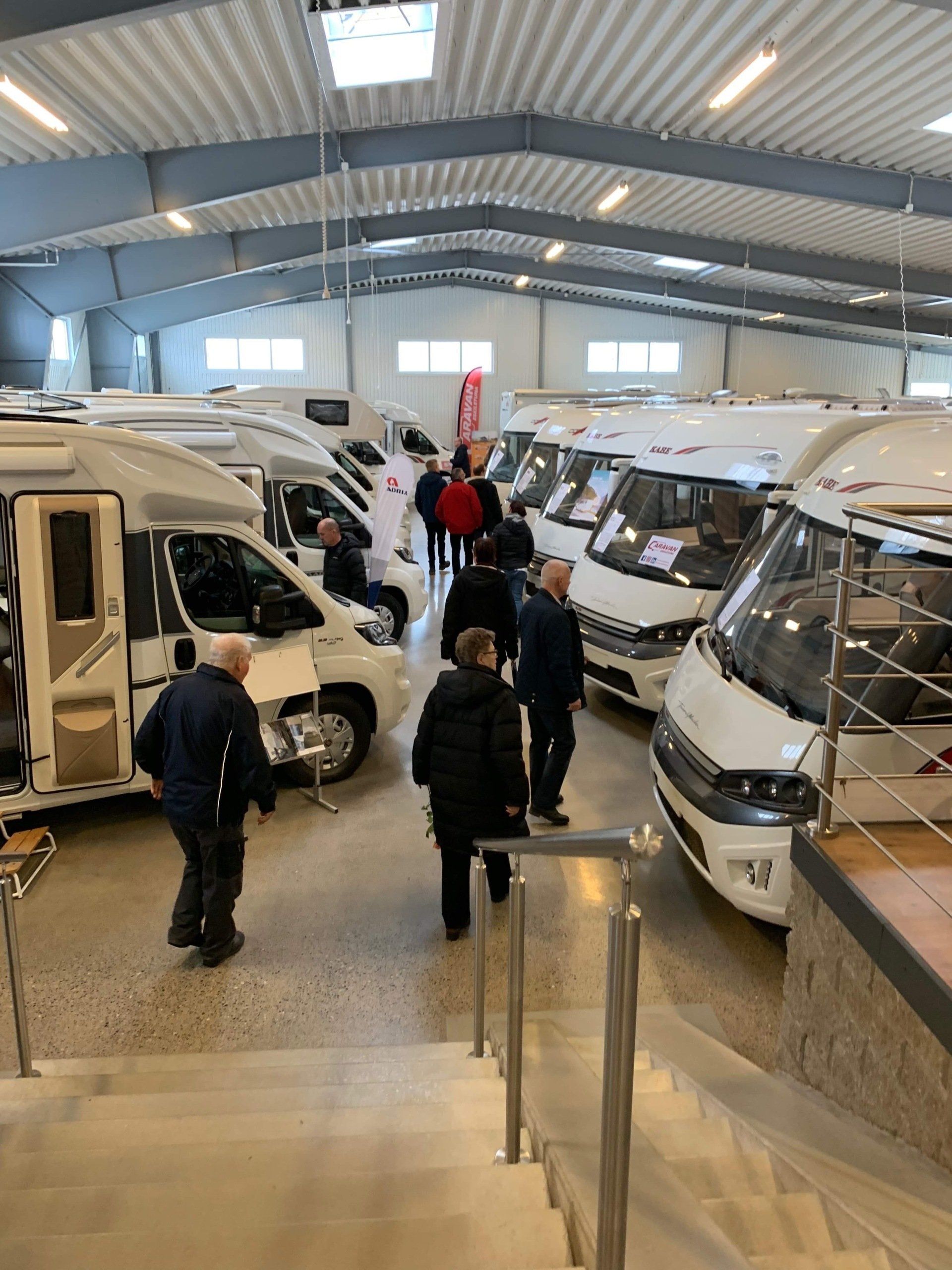 People browse RVs inside a large showroom with bright lighting.