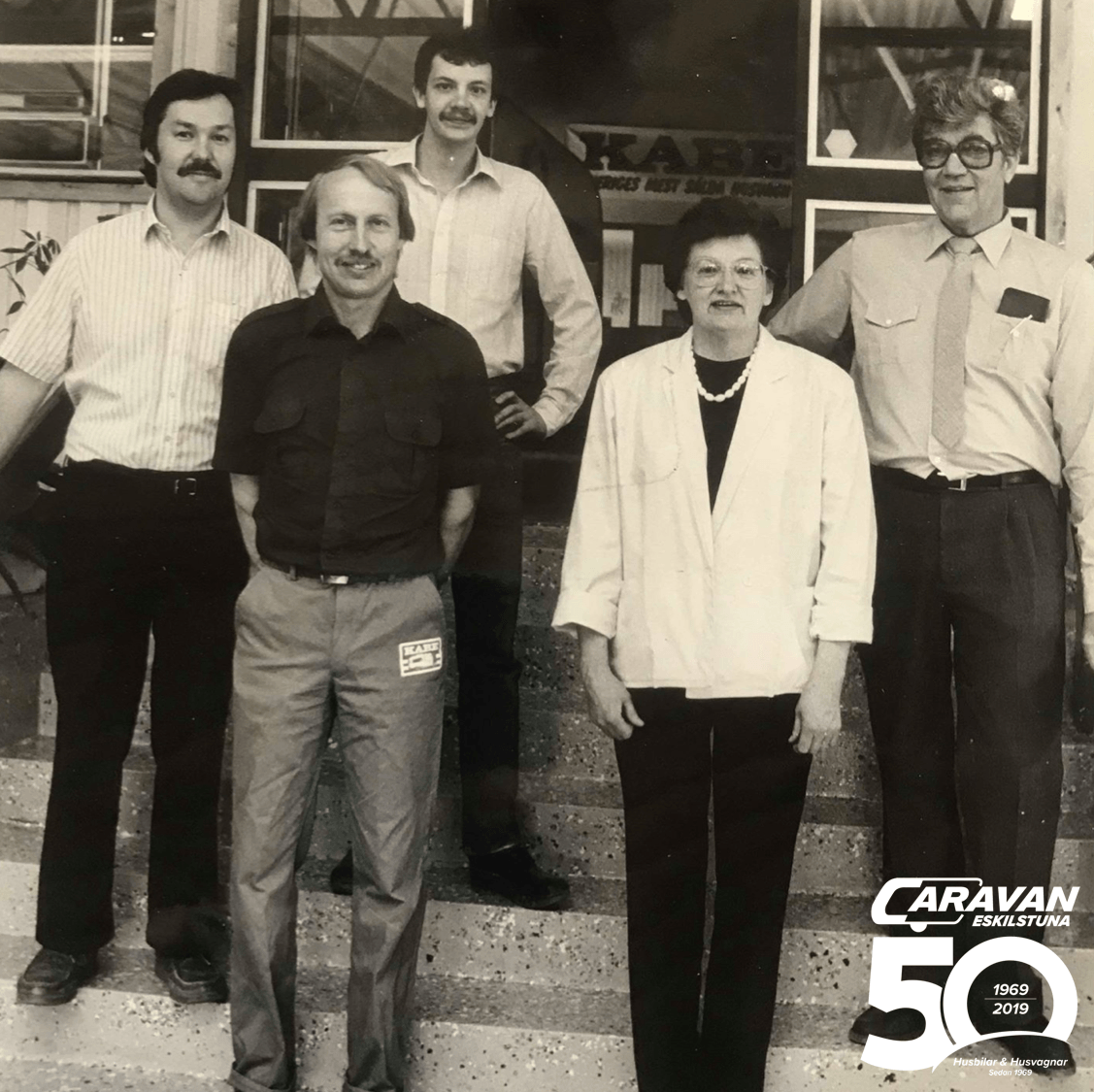 Group of five people standing outside building with the word 