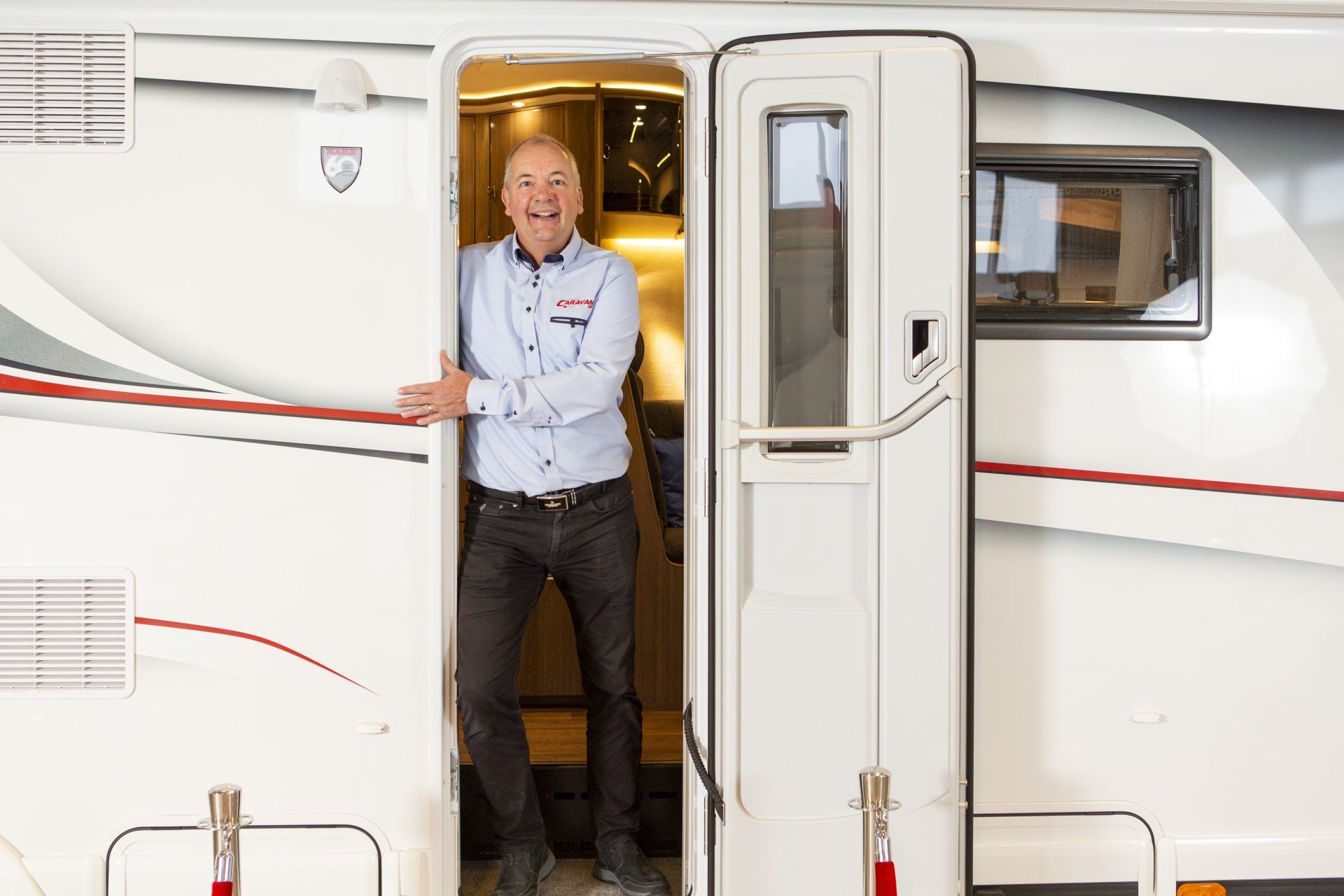 Man in blue shirt and black pants smiles from RV doorway.