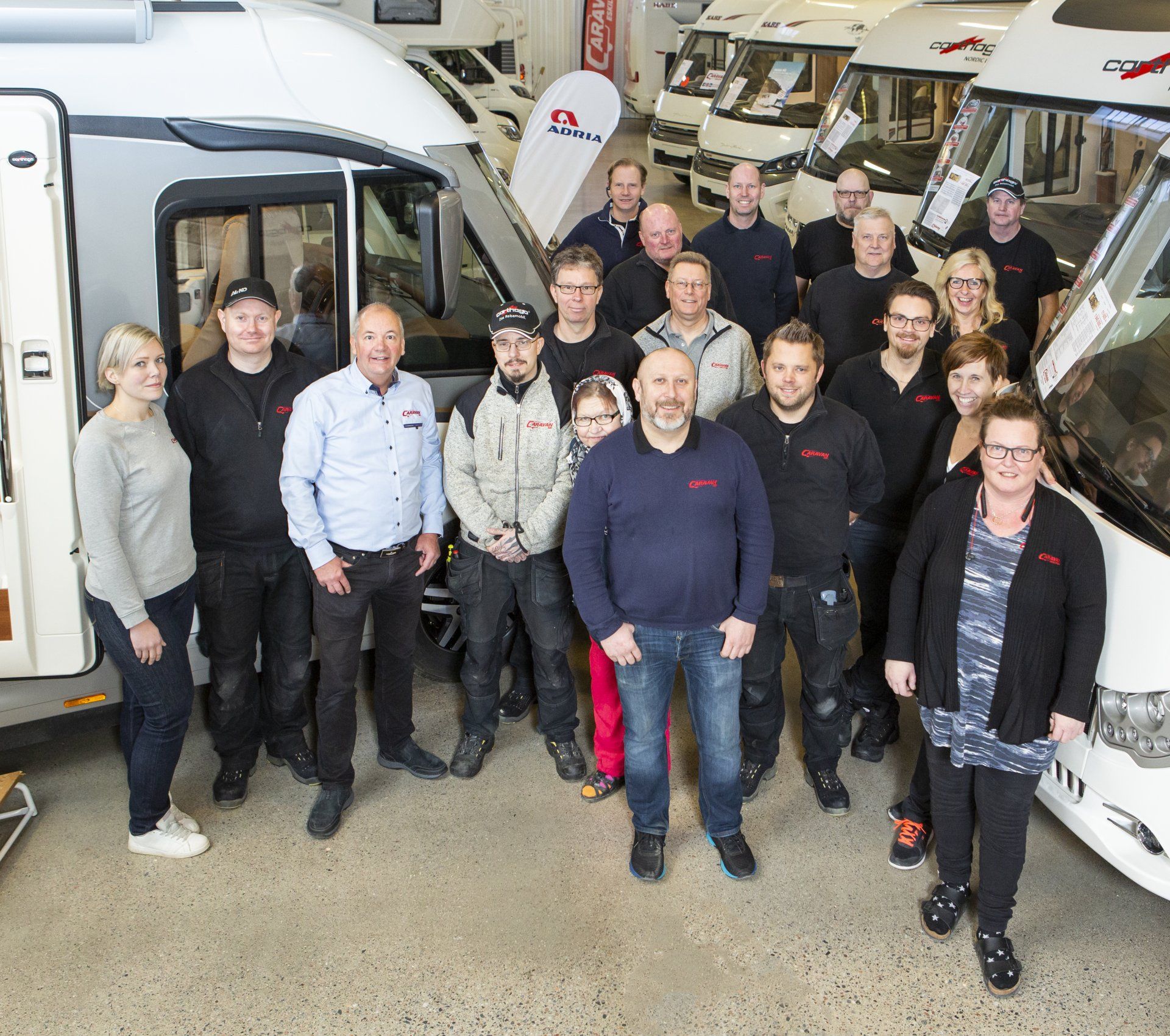 Group of people posing with RVs inside a dealership. Several people in dark shirts.