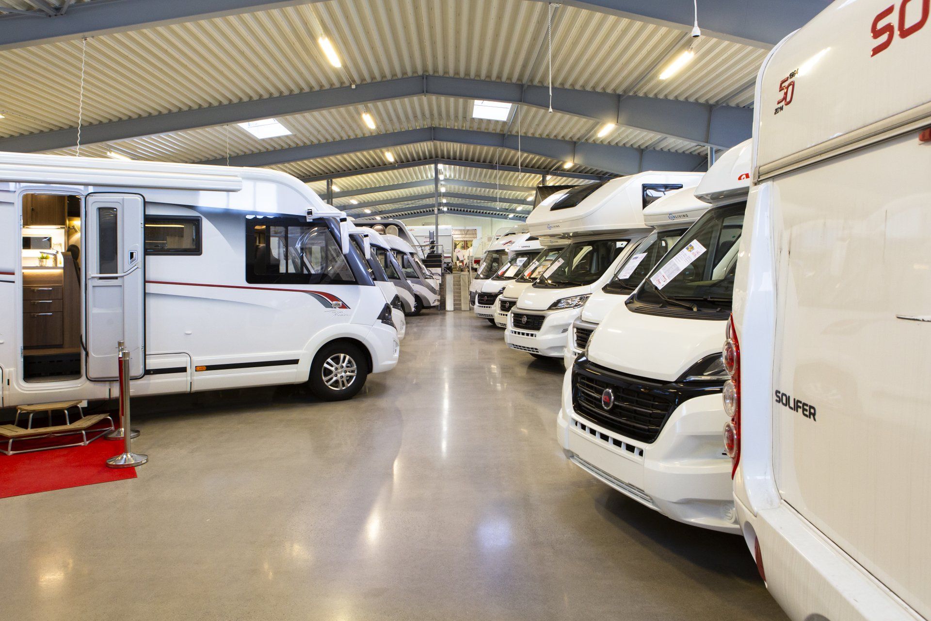 Campers parked inside a bright showroom. White exteriors, red accents, and a reflective floor.
