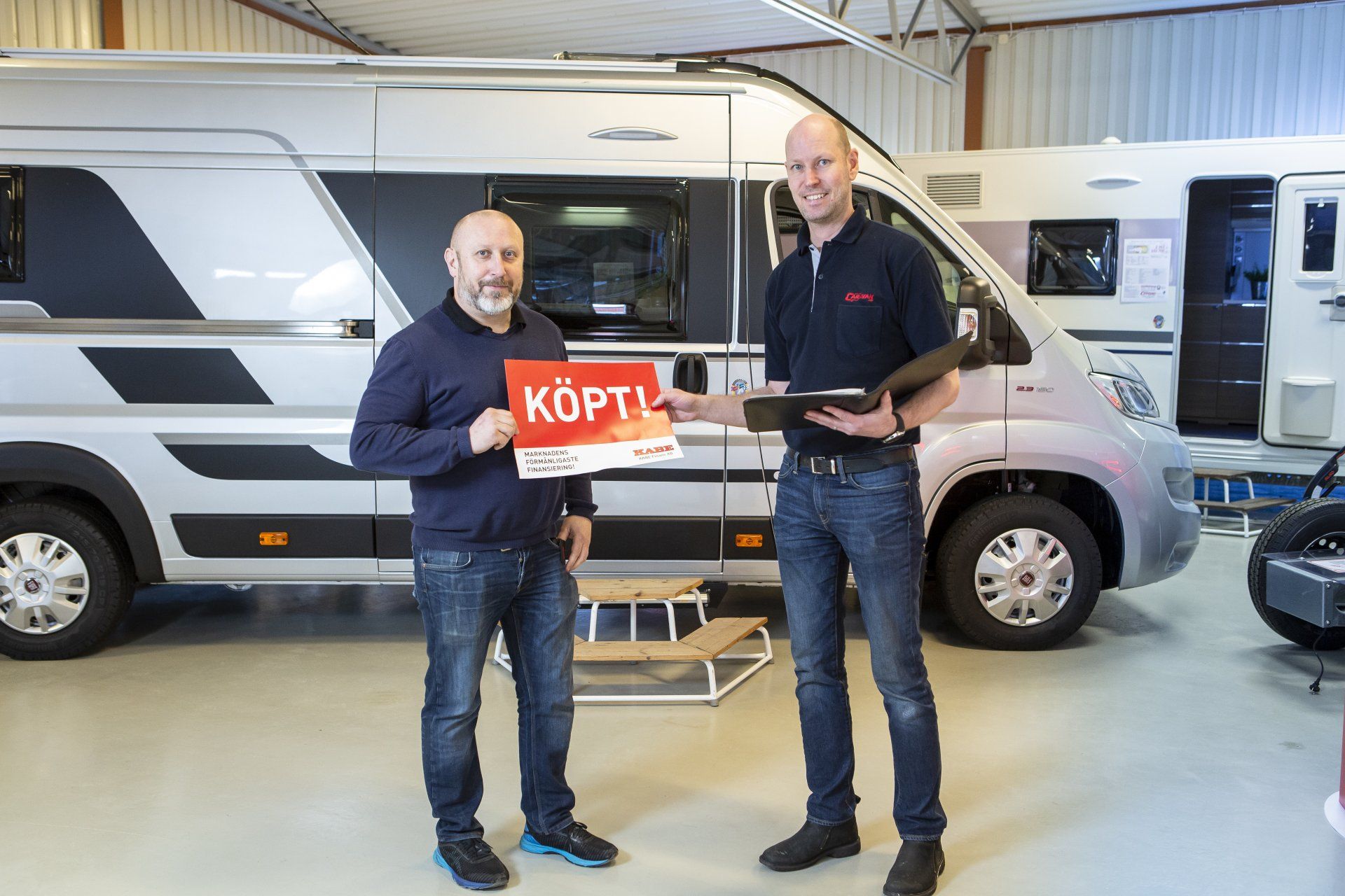 Two men standing by a campervan, one holding a