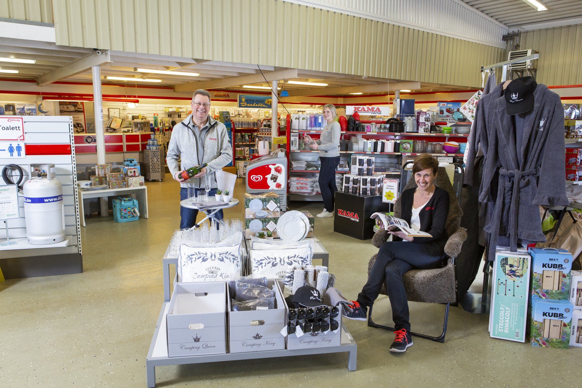 People in a store: one holding items, one reading, one in background. Products on display.