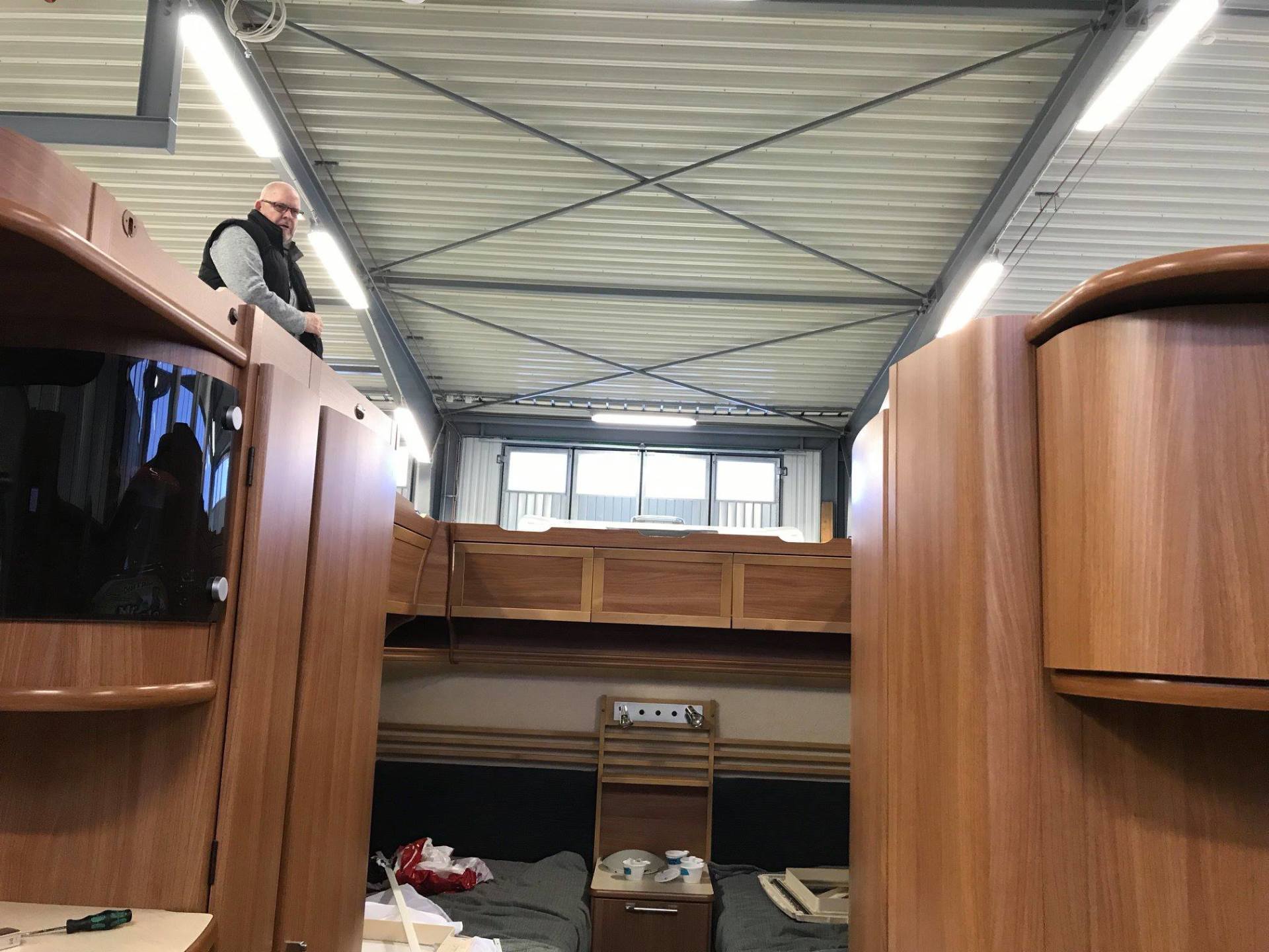 Man standing inside a large cabin with wood paneling; two bunk beds visible.