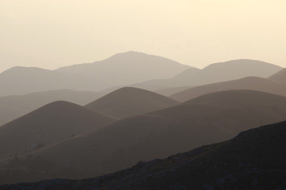Sanfte Hügel in Grau- und Brauntönen und ein blasser Himmel bilden eine vielschichtige Landschaft.