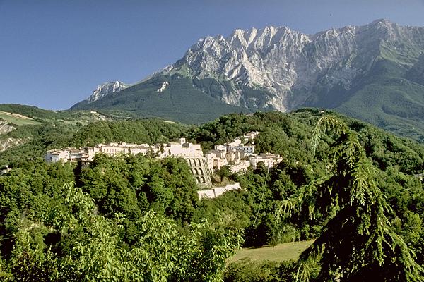 Eine Bergstadt, umgeben von üppigen grünen Bäumen, mit einem großen, schroffen Berg im Hintergrund unter einem blauen Himmel.