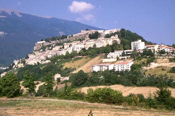 Eine Bergstadt in Italien mit weißen Gebäuden, Bäumen und einer Bergkulisse im Hintergrund.