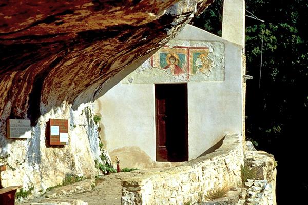 Eine kleine weiße Kirche, die in eine Felshöhle gebaut wurde. Der Eingang hat eine dunkle Tür und darüber verblasste Fresken.