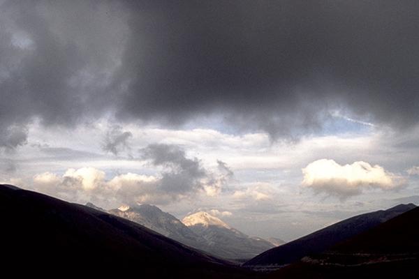 Dunkle, stürmische Wolken über der Bergkette. Sonnenlicht bricht durch die Wolken und beleuchtet ferne Gipfel.