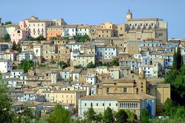 Eine Bergstadt in Italien mit farbenfrohen Gebäuden, einem Kirchturm und üppigen grünen Bäumen.