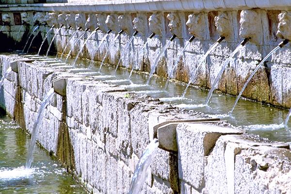 Steinbrunnen mit vielen Ausgüssen, die jeweils die Form eines menschlichen Gesichts haben 