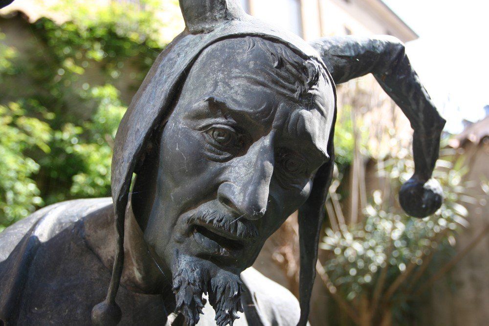 Bronzestatue eines Narren mit gerunzelter Stirn und traurigem Gesichtsausdruck, im Freien.