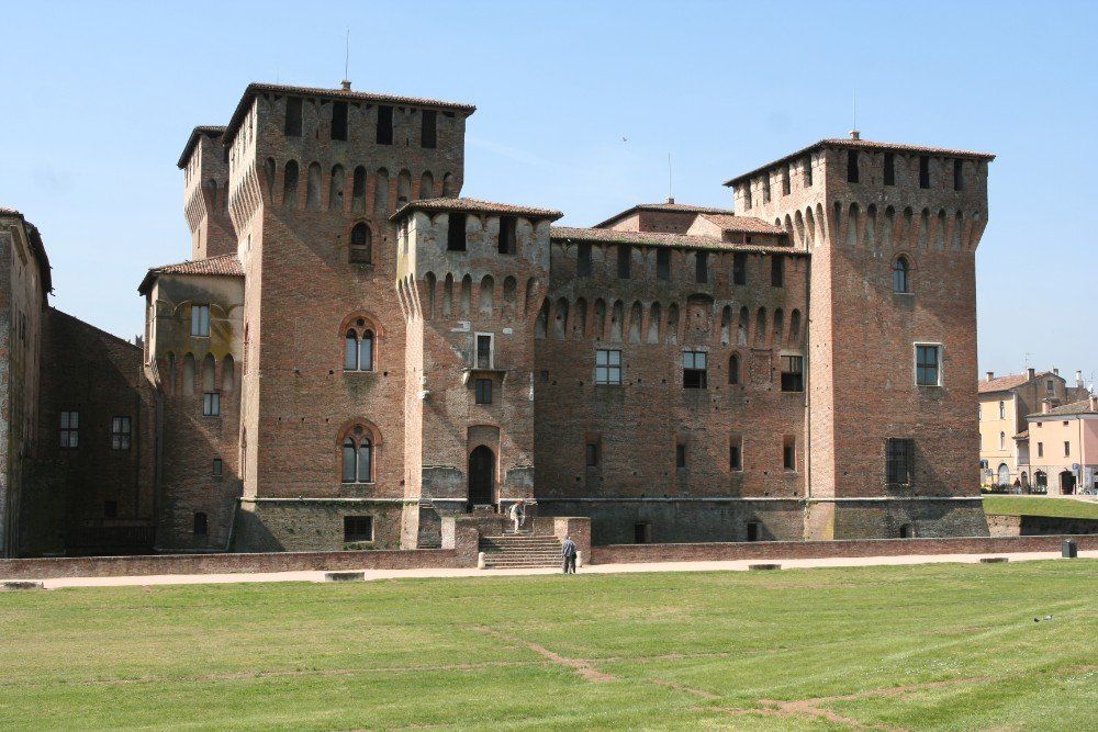 Backsteinschloss mit quadratischen Türmen auf einem grünen Rasen unter blauem Himmel. 