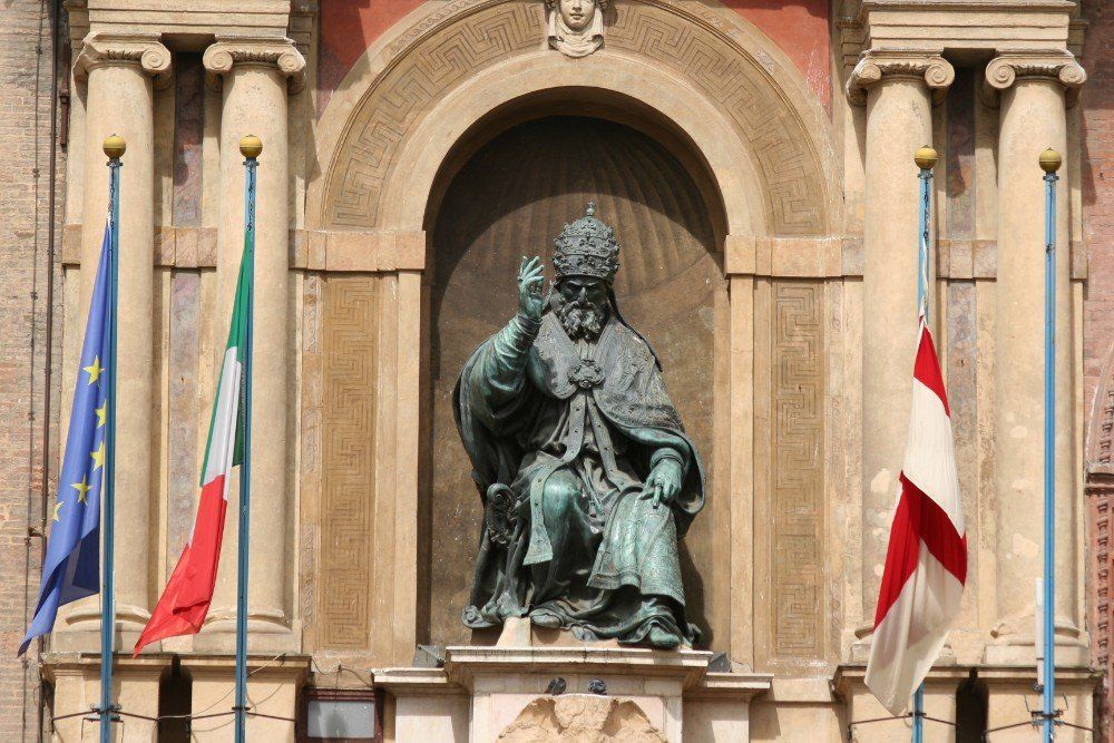 Statue von Papst Gregor XIII. in Bologna, Italien, mit Flaggen der EU, Italiens und der jeweiligen Stadt auf beiden Seiten.