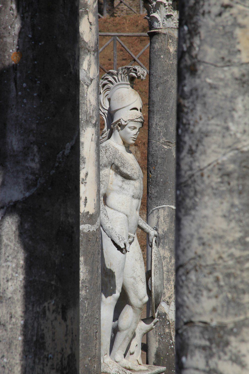 Steinstatue eines Mannes in römischer Rüstung, der einen Stab hält, zwischen Säulen.