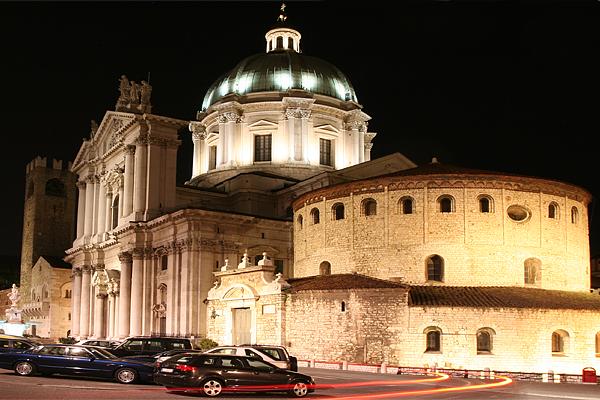 Nachtansicht der Piazza Paolo VI in Brescia mit der Neuen Kathedrale, der Alten Kathedrale und geparkten Autos. 