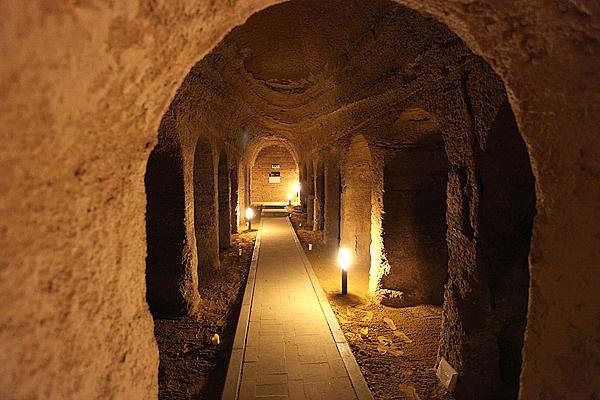 Tunnel mit gewölbter Decke und Säulen, beleuchtet durch Lichter, die einen Weg durch die Dunkelheit schaffen.