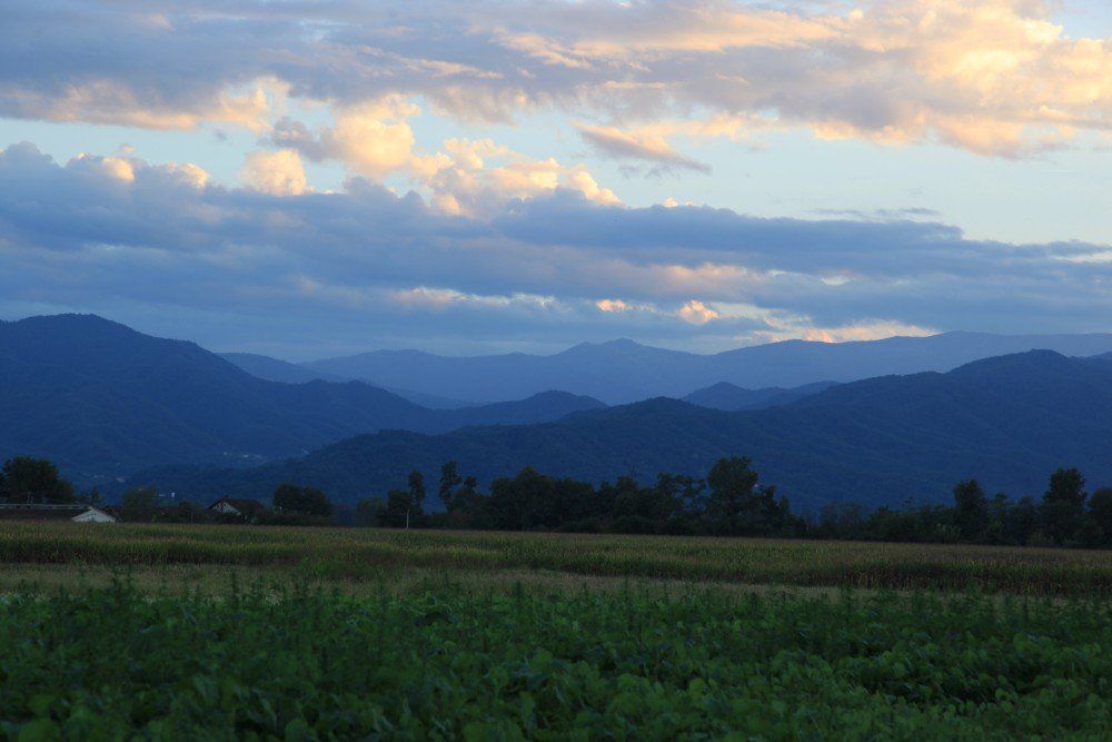 Blaue Bergkette unter bewölktem Himmel in der Abenddämmerung. Grünes Feld im Vordergrund.
