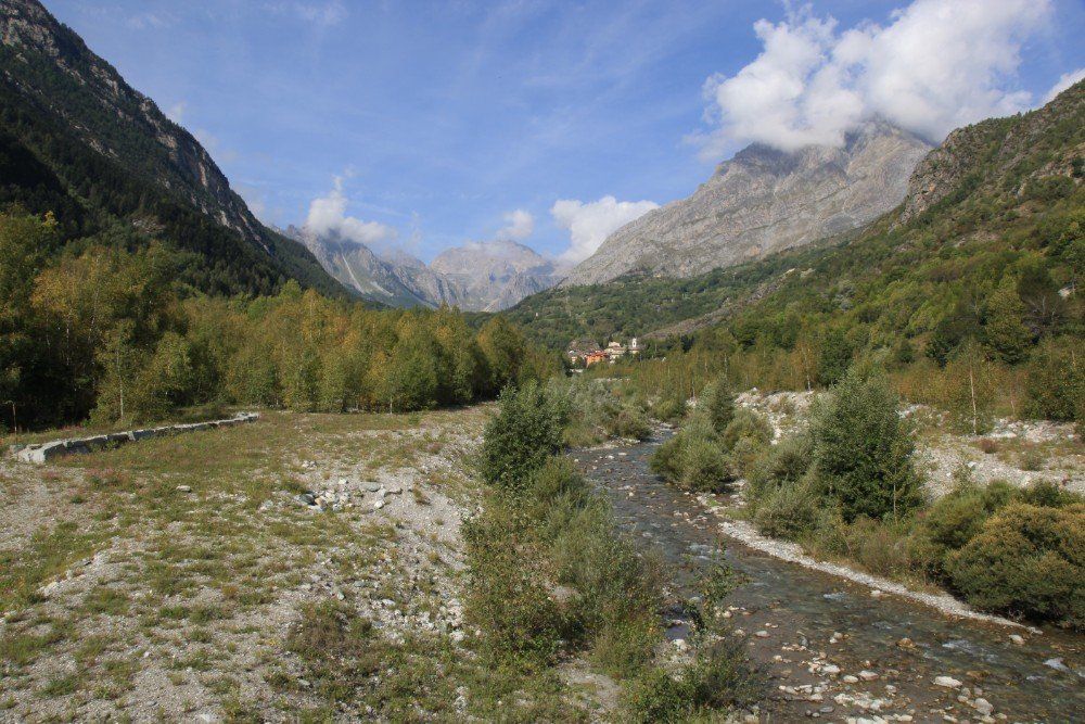 Fluss, der durch ein Tal fließt, flankiert von Bergen und Bäumen unter einem teilweise bewölkten Himmel.