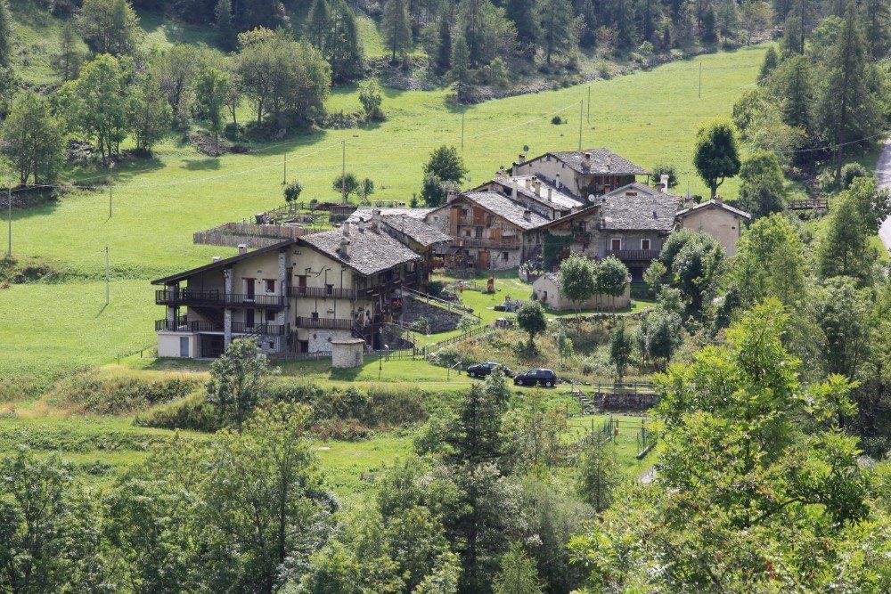 Ein Dorf mit Stein- und Holzhäusern, eingebettet in ein grünes Tal, umgeben von Bäumen und Hügeln.