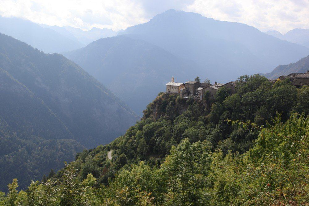 Ein Gebäude auf einer grünen Klippe mit Blick auf eine Berglandschaft. Im Hintergrund sind dunstige Berge zu sehen.