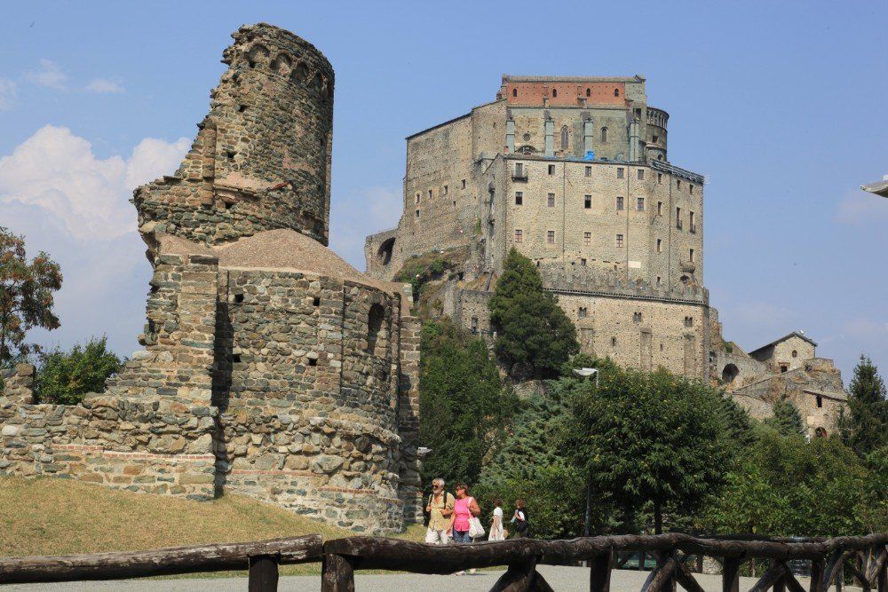 Mittelalterliches Kloster auf einem felsigen Hügel in Italien, mit Steinruinen im Vordergrund und Touristen